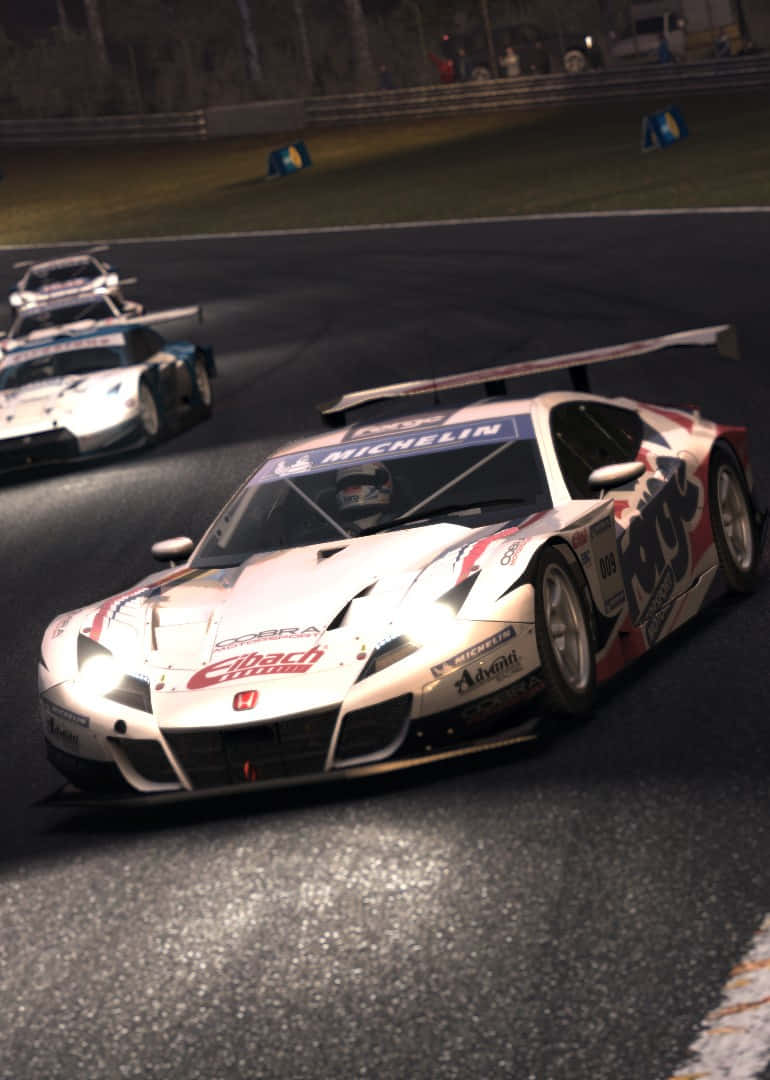 iPhone X Grid Autosport 桌布 壁紙 — 一輛帶有紅色和藍色貼紙的白色賽車在夜間濕滑的賽道上疾馳，後面還有一輛車緊隨其後。