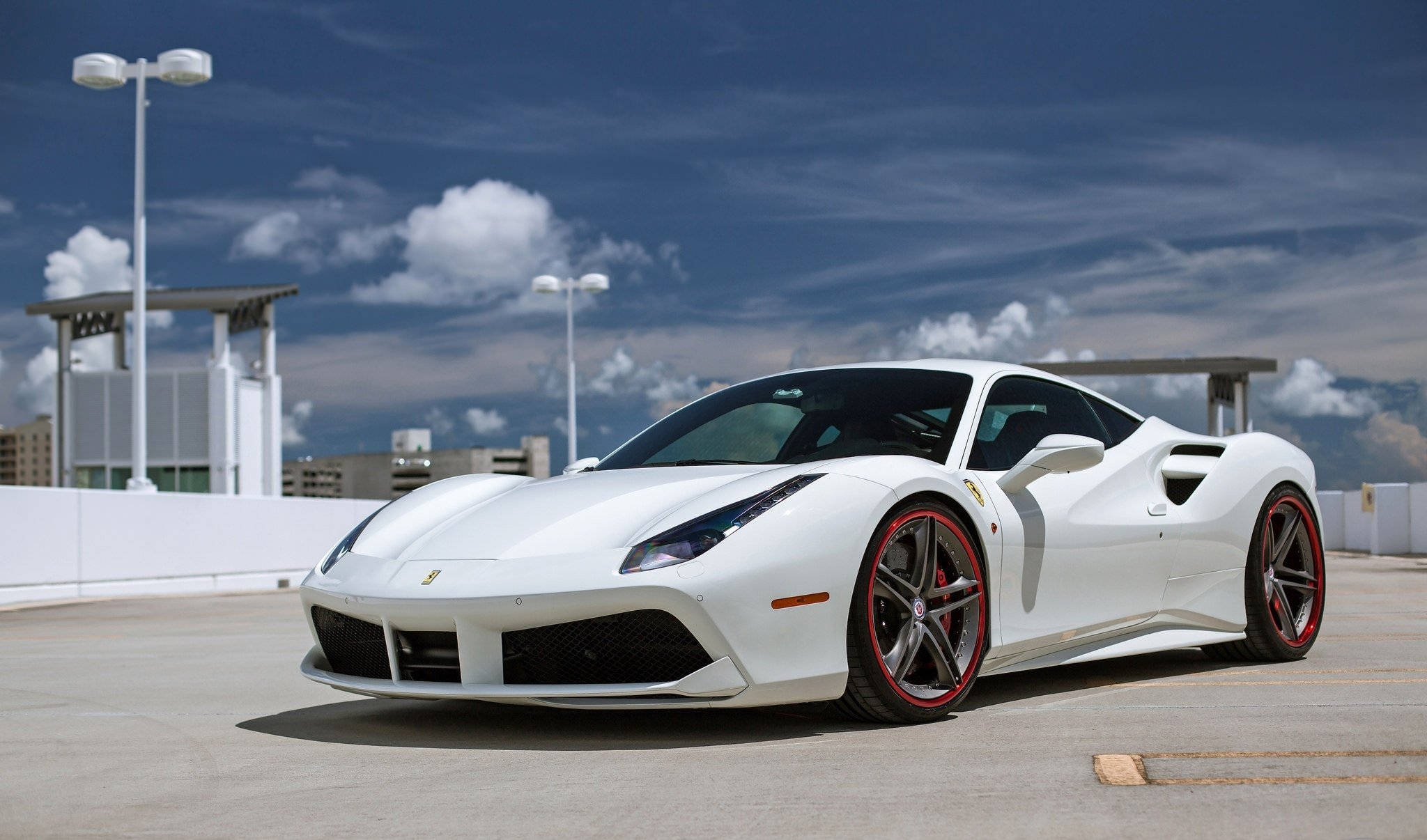 white ferrari 桌布 壁紙 — 一輛帶有紅色輪圈的純白色法拉利跑車停在天台上，背景是帶有蓬鬆雲朵的戲劇性藍天。