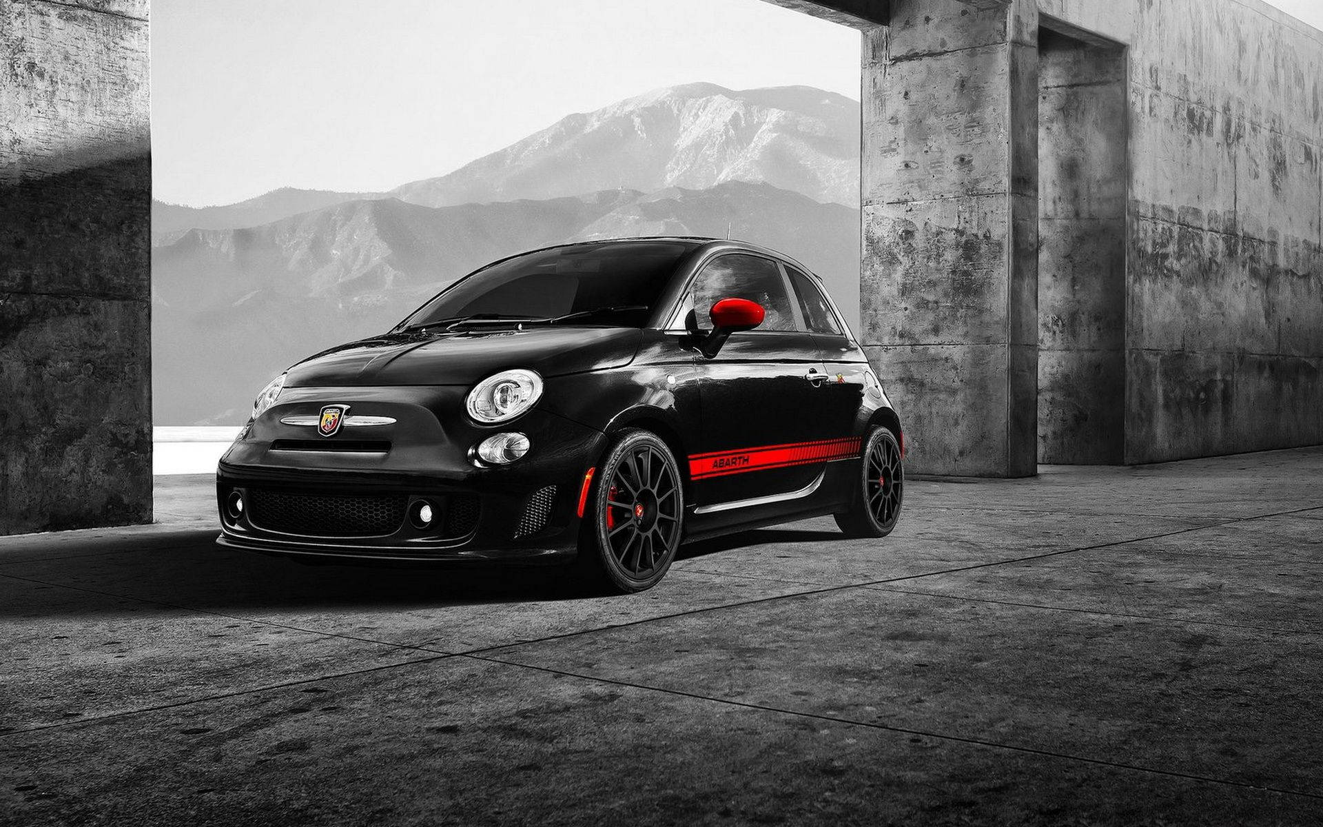 Fiat 桌布 壁紙 — 一輛帶有紅色飾邊的黑色Fiat 500 Abarth停在混凝土拱門下，背景是雪山。