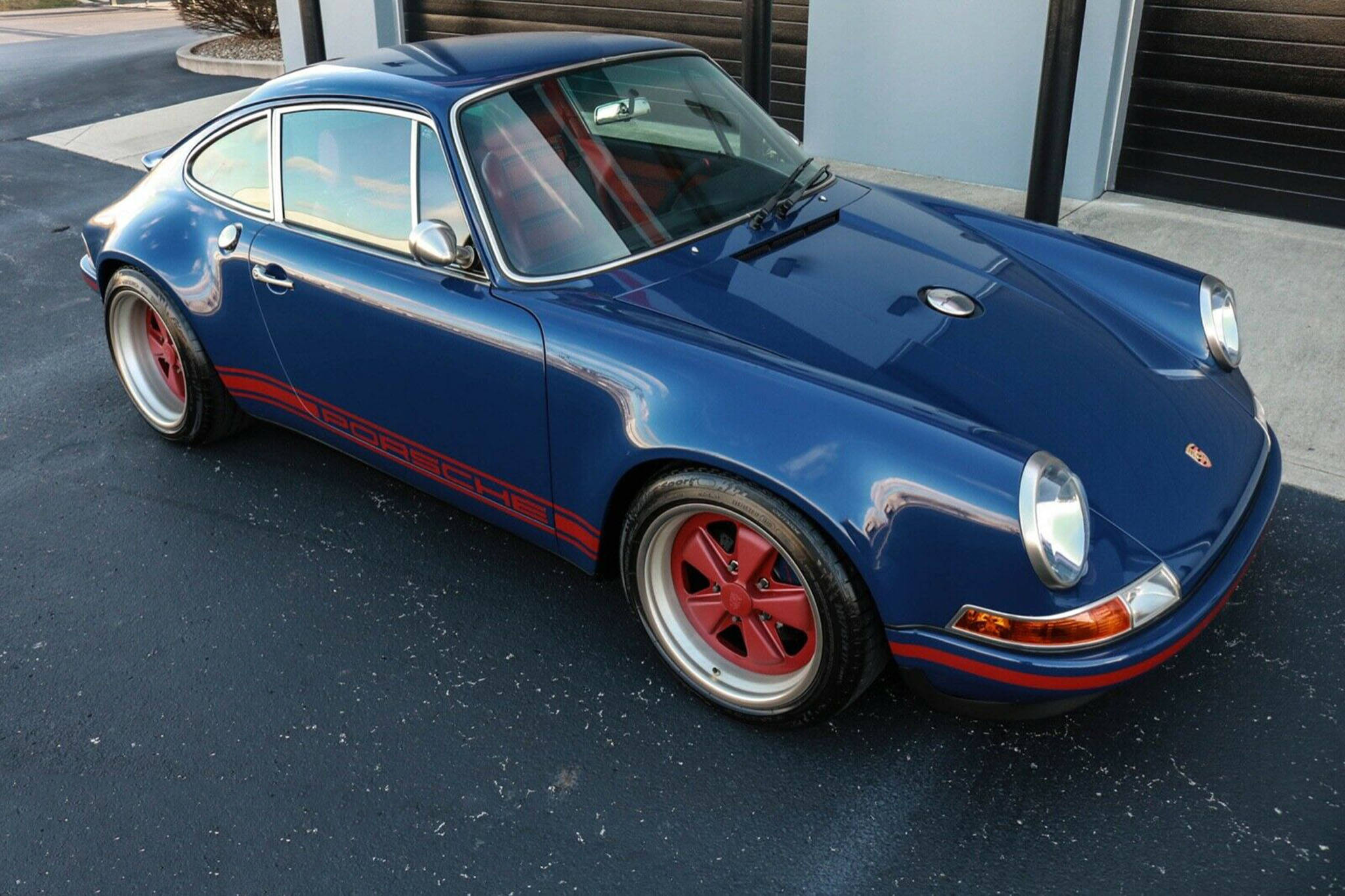Singer 桌布 壁紙 — 一輛帶有紅色點綴和輪轂的光澤藍色保時捷911停在建築物附近的瀝青路面上。