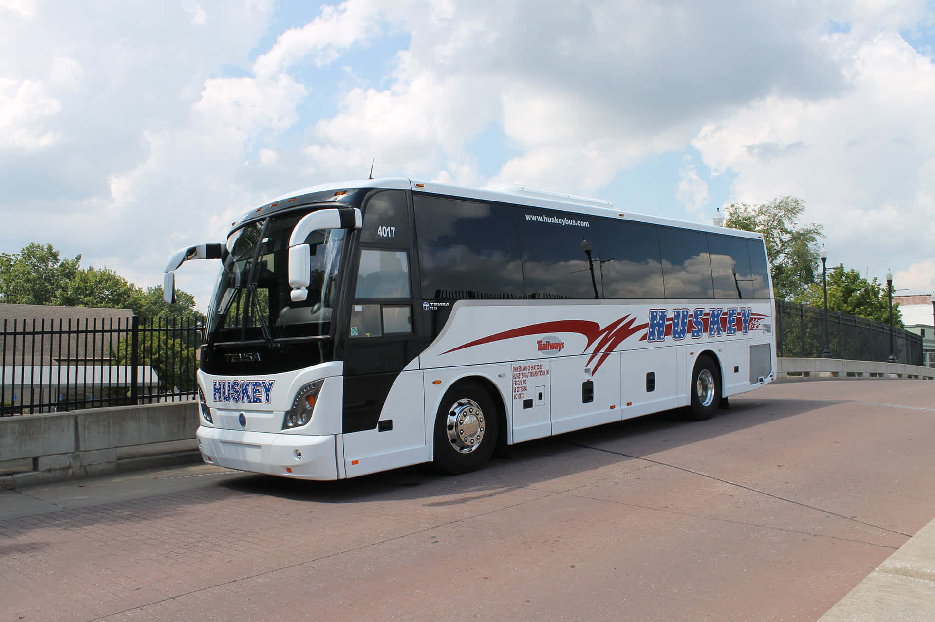 Bus 桌布 壁紙 — 一輛帶有紅色點綴的時尚白色Huskey旅遊巴士停在鋪砌的道路上，天空部分多雲。