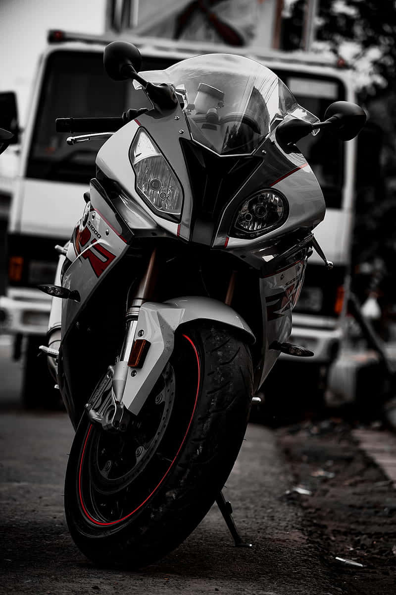 Superbike 桌布 壁紙 — 一輛帶有紅色點綴的時尚白色運動機車，停在一條粗糙街道的側腳架上，其銳利的線條和進取的姿態通過選擇性色彩凸顯出來。