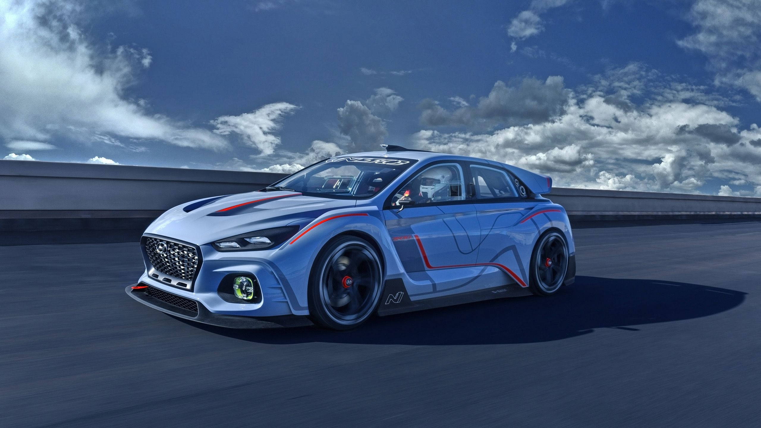 Hyundai 桌布 壁紙 — 一輛帶有紅色點綴的時尚藍色賽車在戲劇性的多雲天空下沿著高速公路飛馳。