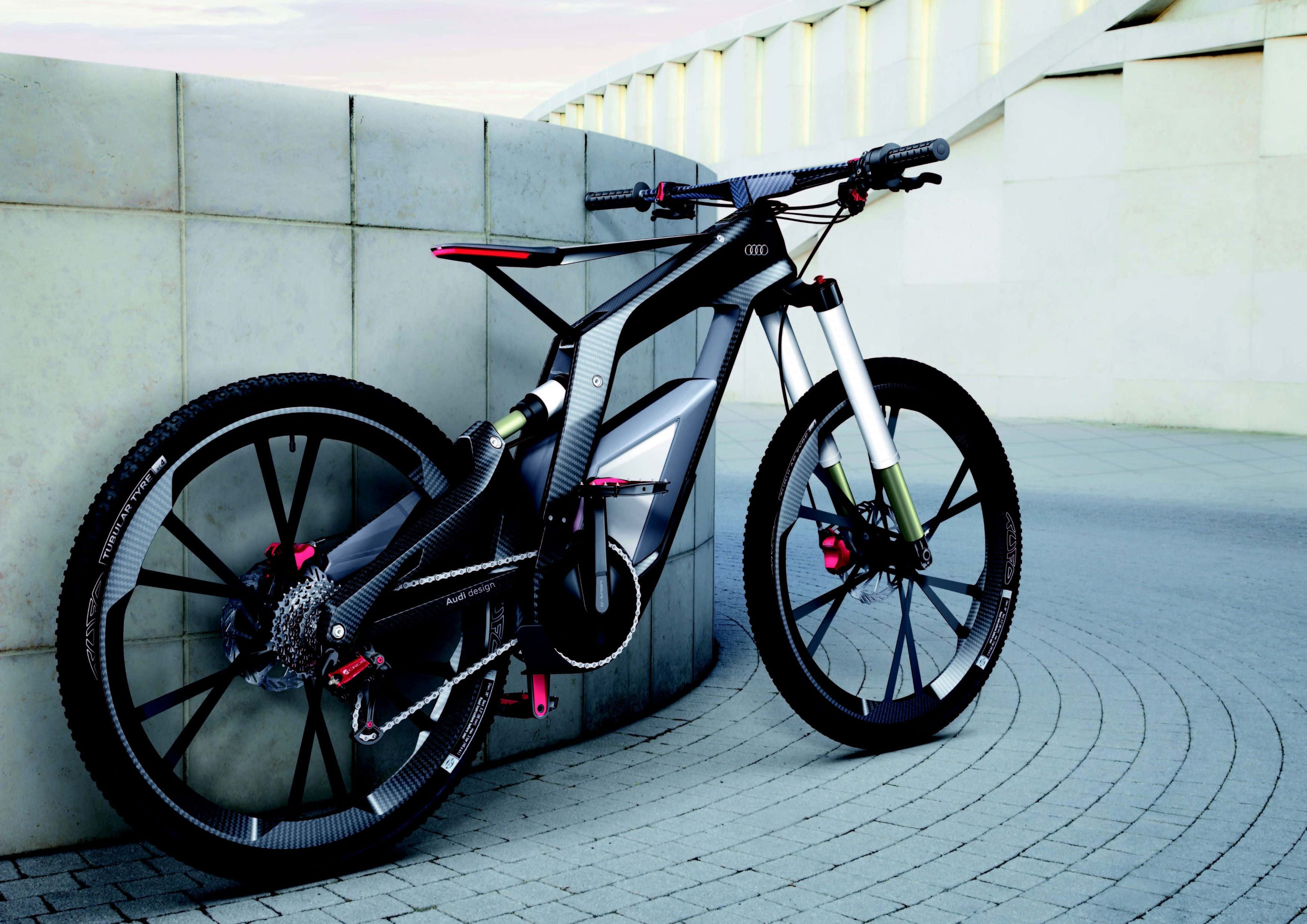 Electric Bike 桌布 壁紙 — 一輛帶有紅色點綴的時尚黑色Audi電動登山車，在黃昏時靠在瓷磚廣場的弧形混凝土牆上。