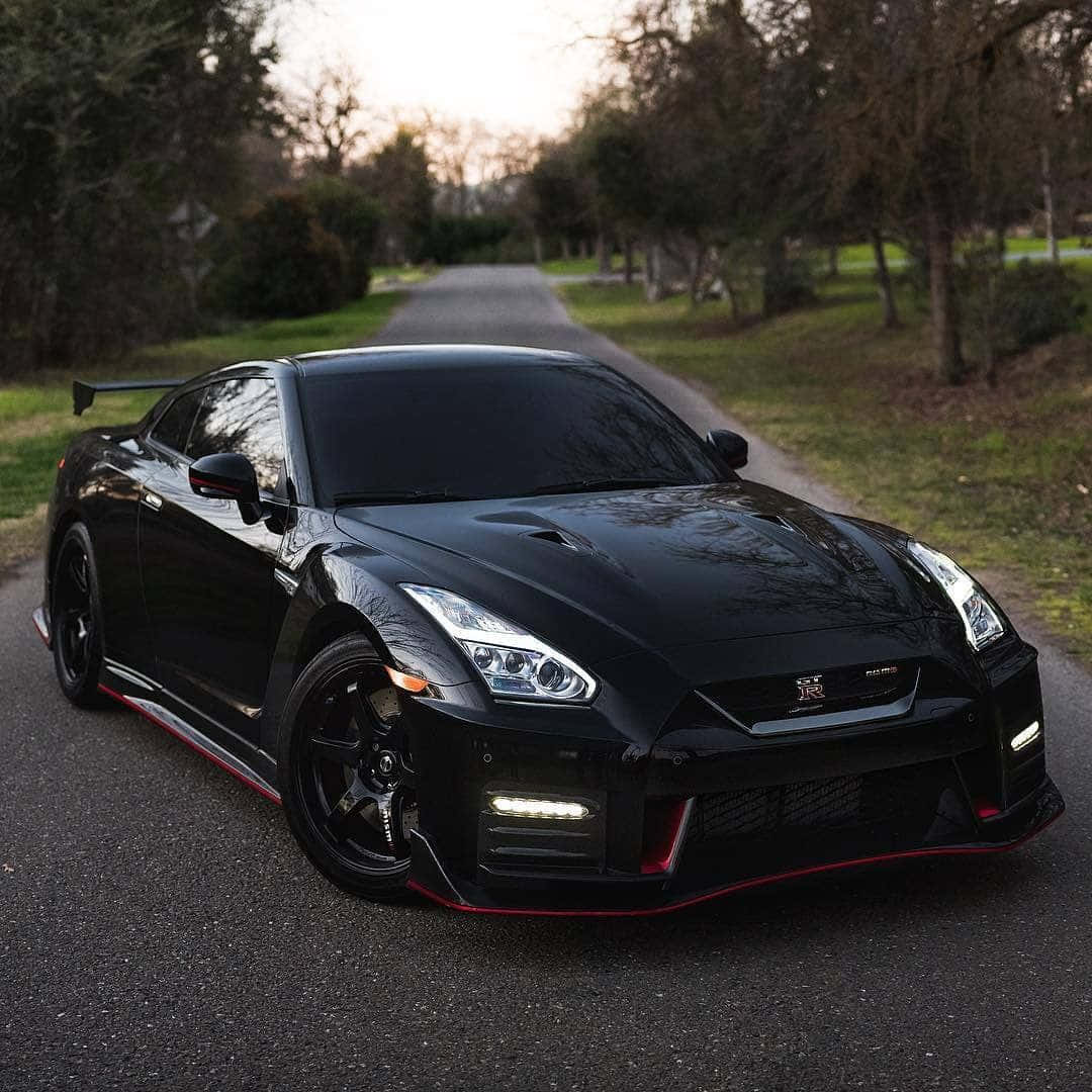 Nissan 桌布 壁紙 — 一輛帶有紅色點綴的時尚黑色日產GT-R，在黃昏時停泊在綠樹成蔭的道路上。