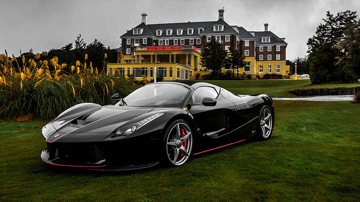 跑車 桌布 壁紙 — 一輛帶有紅色點綴的時尚黑色法拉利 LaFerrari 停放在修剪整齊的草坪上，前方是一座宏偉的黃色酒店，天空多雲。