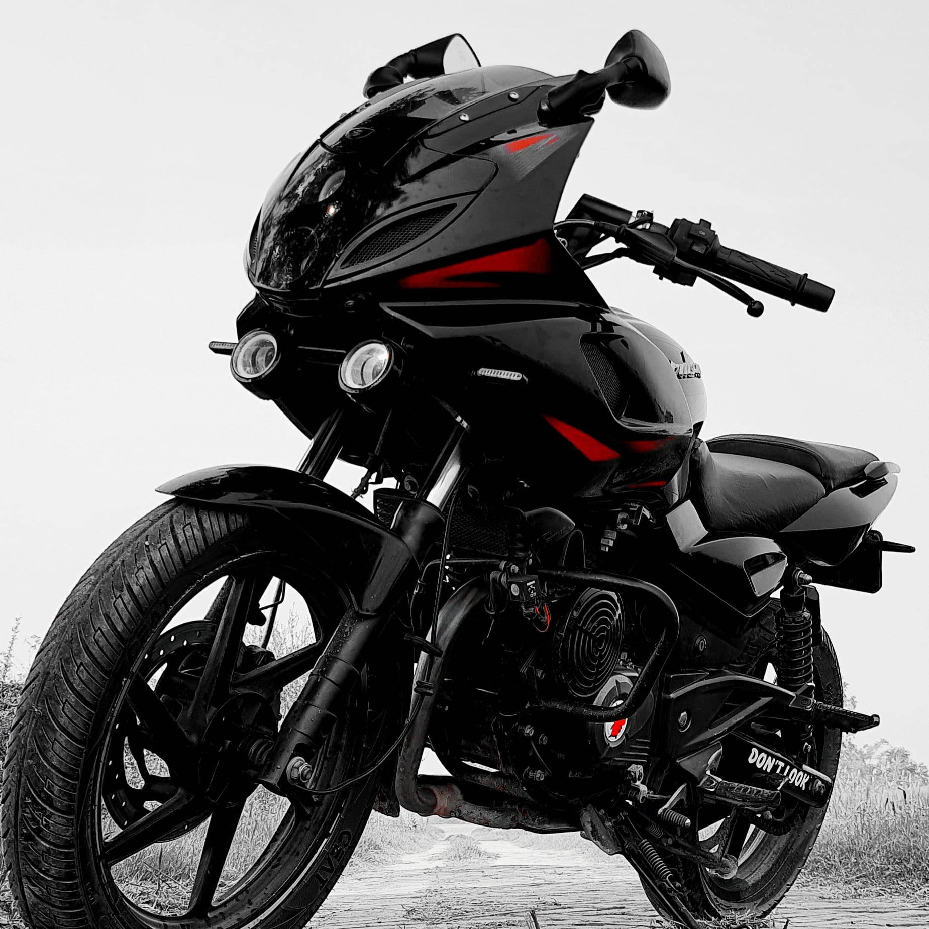 Pulsar 220 HD 桌布 壁紙 — 一輛帶有紅色點綴的時尚黑色運動機車，在單色天空下的碎石路上蓄勢待發。