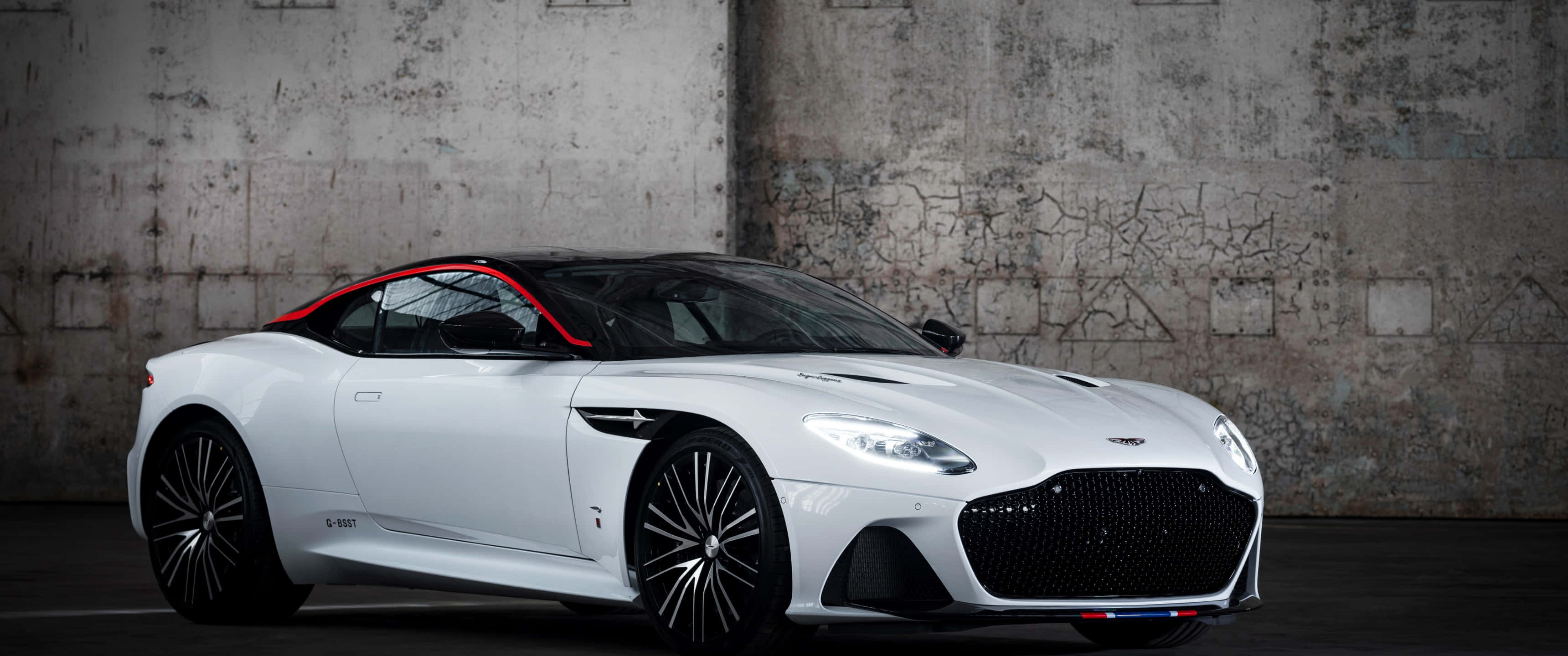 Aston Martin Dbs Superleggera 桌布 壁紙 — 一輛帶有紅色點綴的流線型白色Aston Martin DBS Superleggera，停放在風化的混凝土牆前。