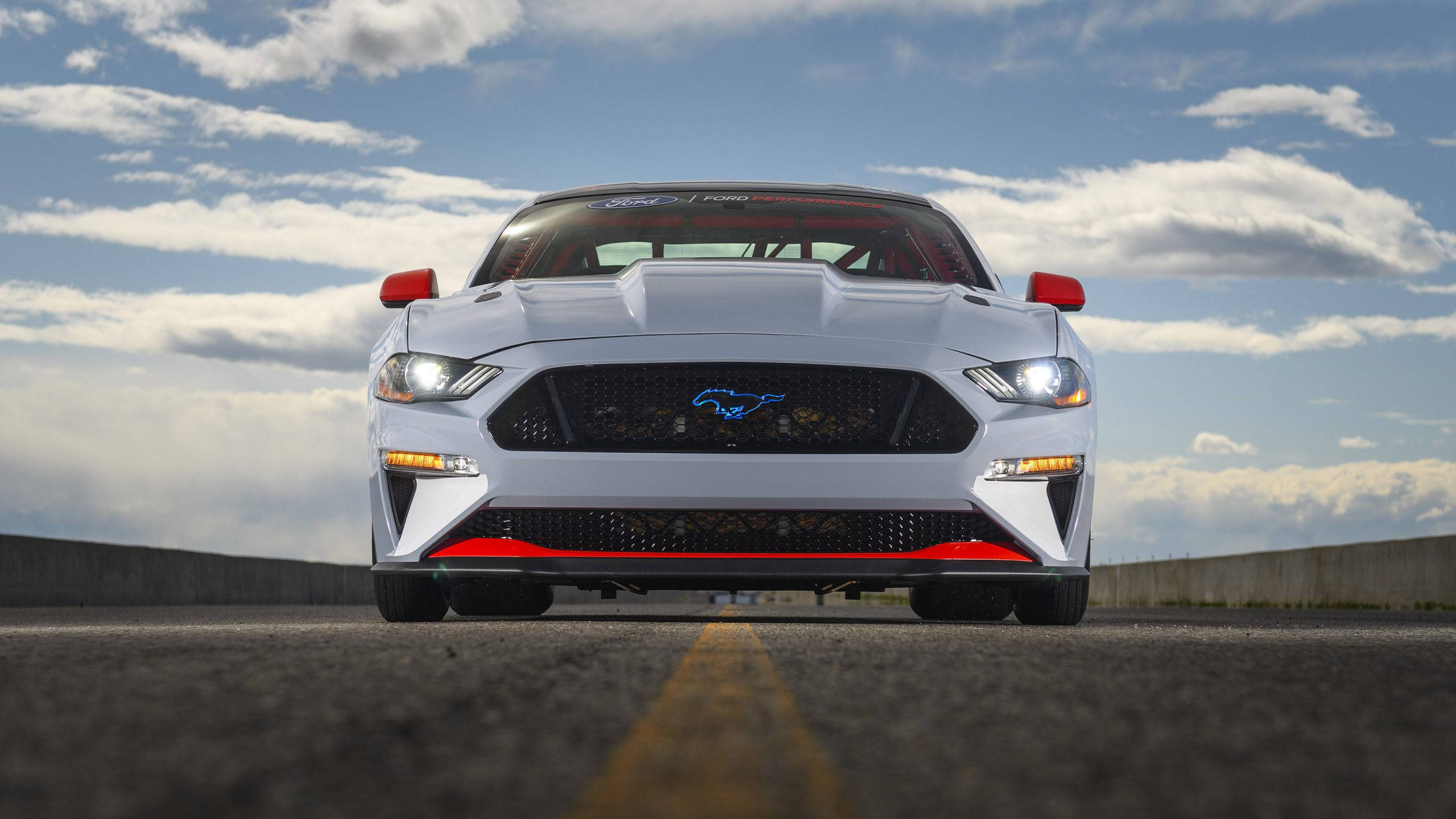 Cool Mustang 桌布 壁紙 — 一輛帶有紅色點綴的白色福特野馬在部分多雲的天空下於賽道上向前行駛。