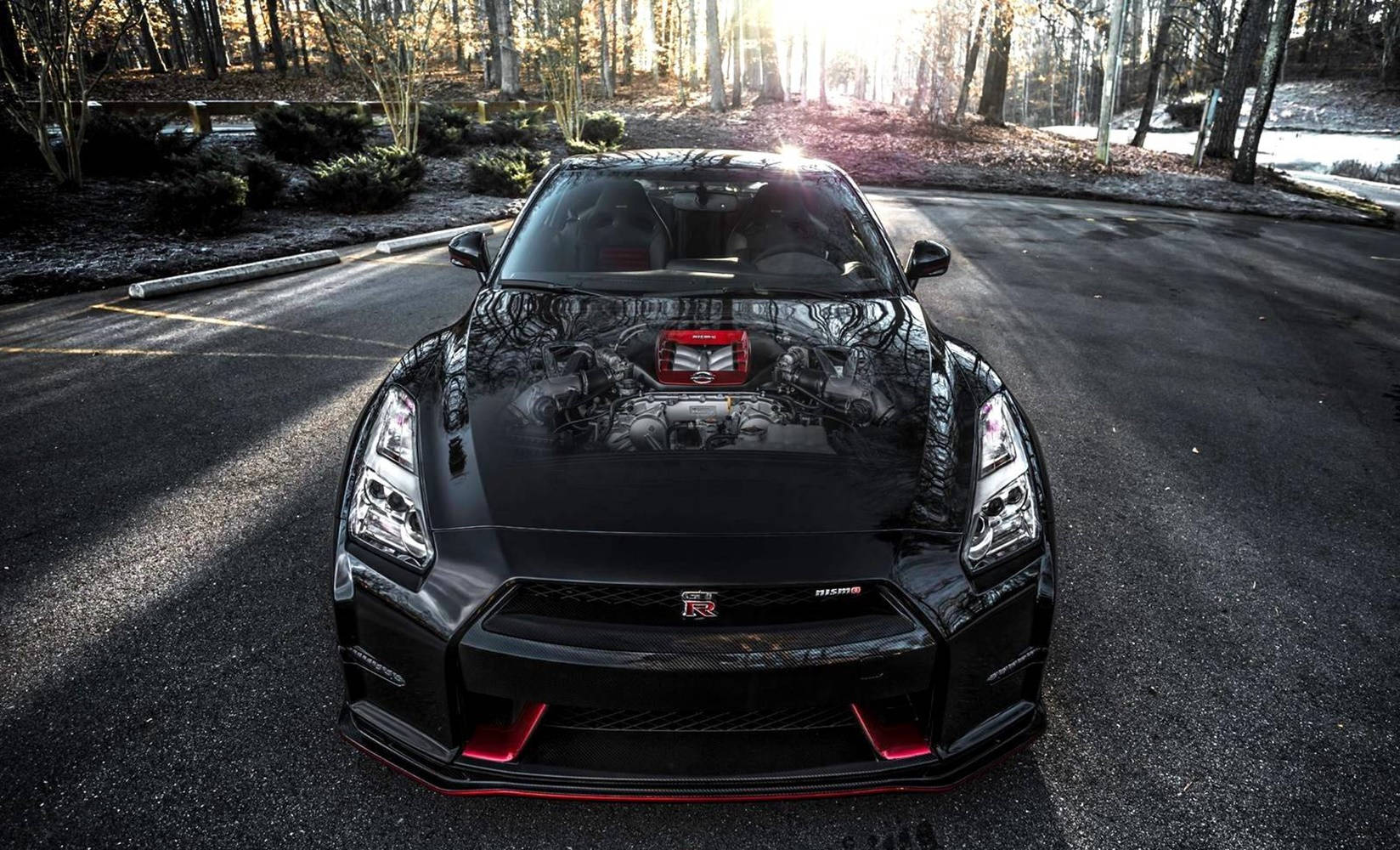 Nissan 桌布 壁紙 — 一輛帶有紅色點綴的黑色日產GT-R停在森林道路上，正值黃金時刻，陽光穿過樹木。