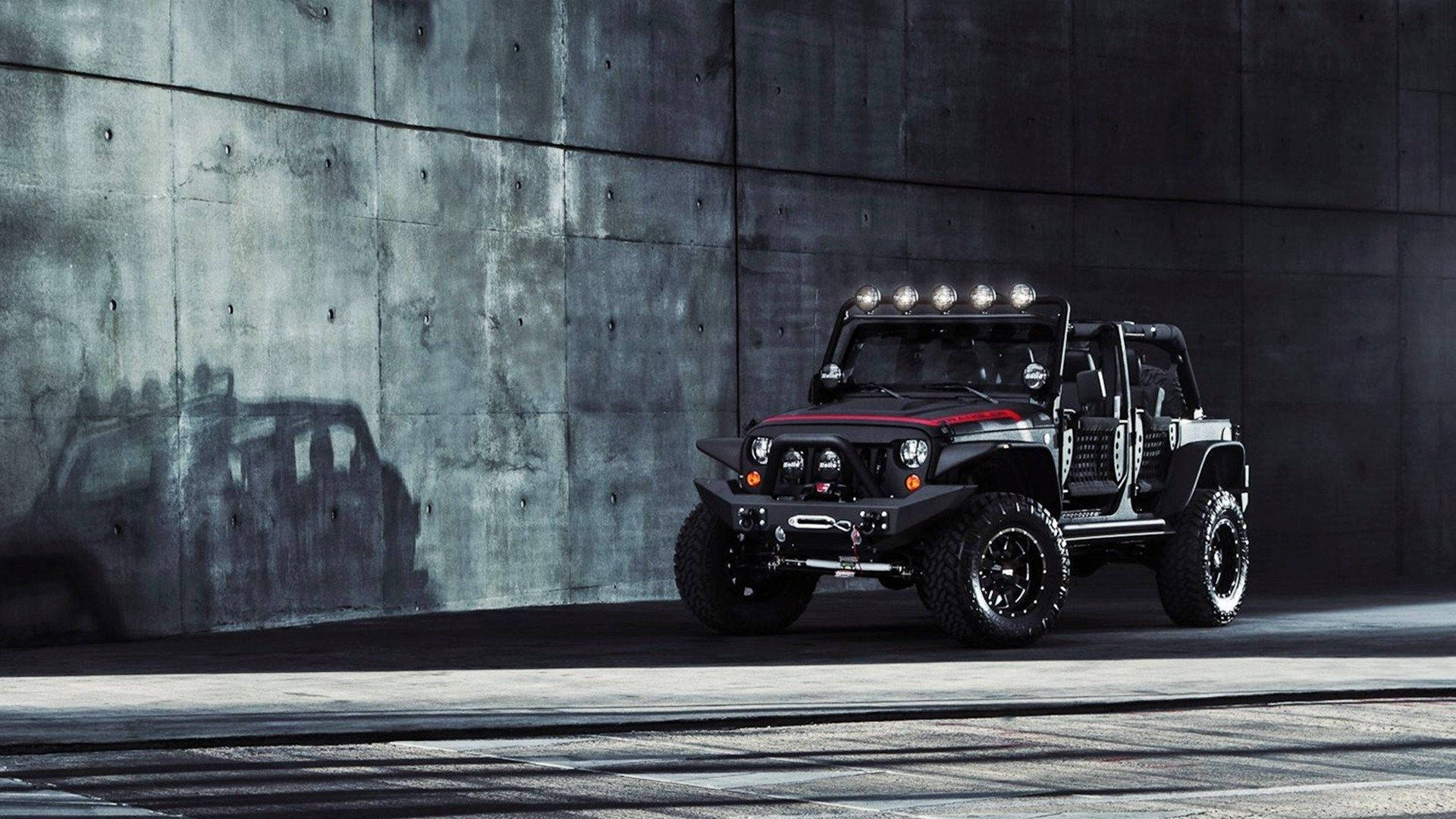 黑色吉普車 桌布 壁紙 — 一輛帶有紅色點綴的黑色越野Jeep在戲劇性燈光下，大膽地停靠在紋理混凝土牆前。