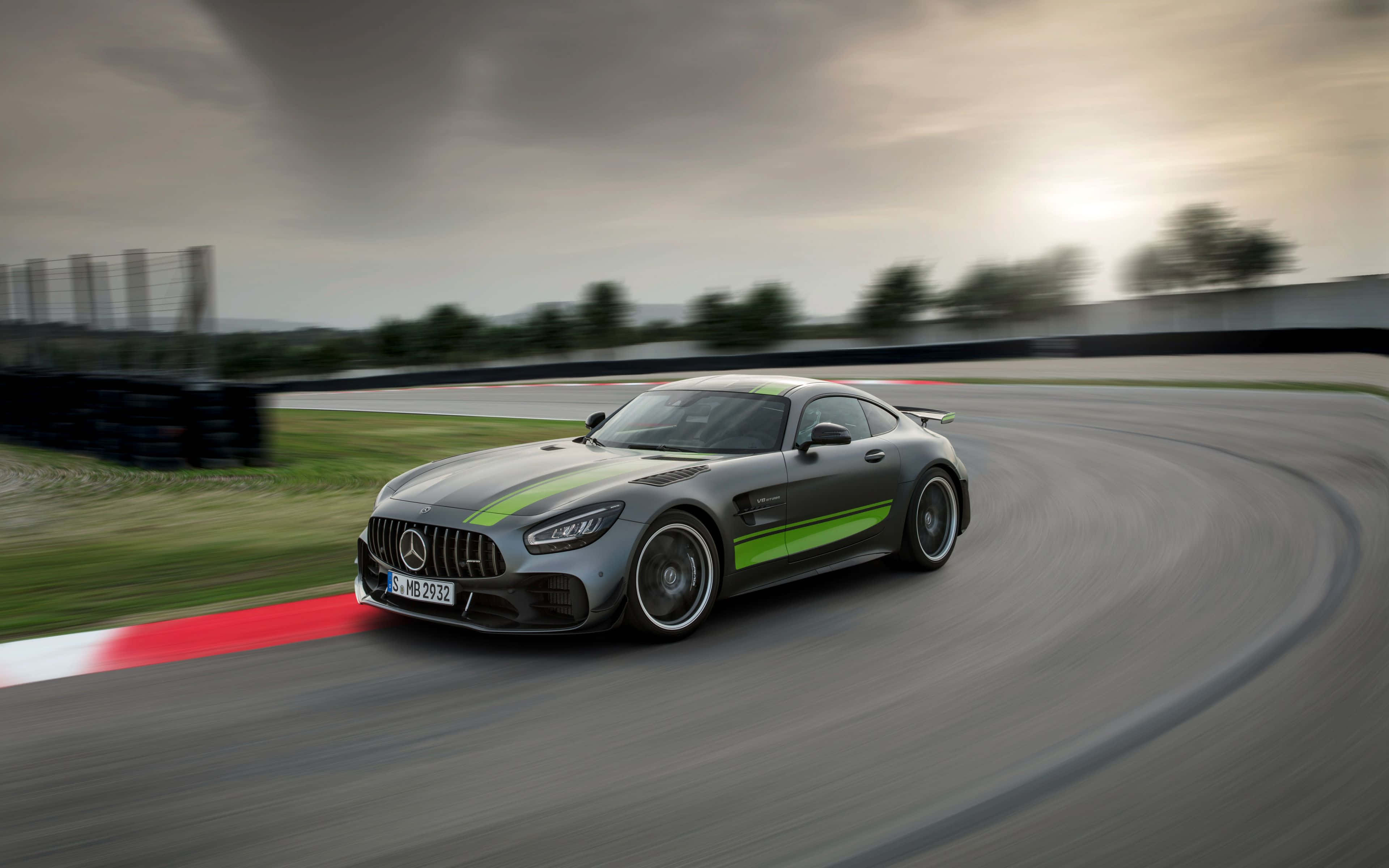 桌布 壁紙 — 一輛帶有綠色條紋的時尚灰色 Mercedes-AMG GT 在多雲的天空下繞著彎曲的賽道奔馳。