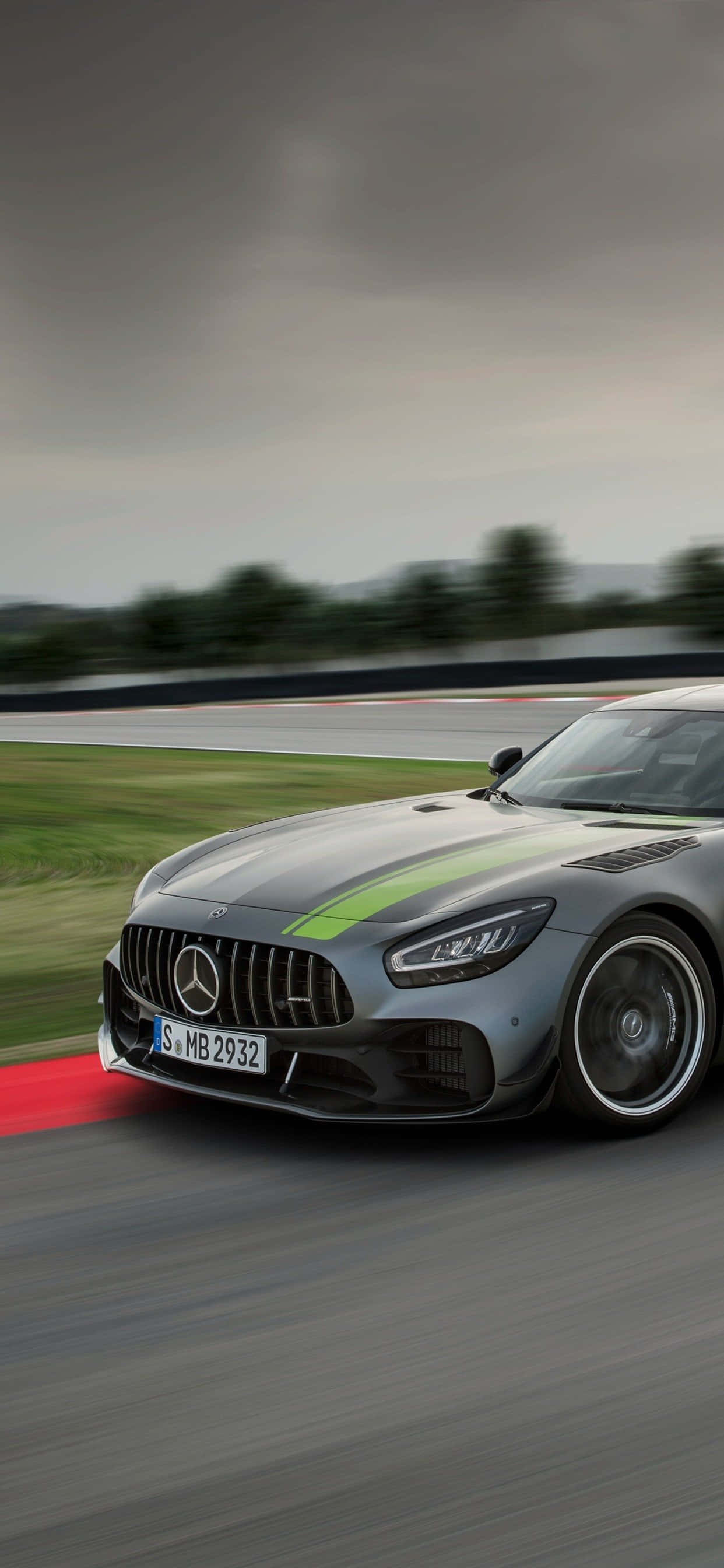 Mercedes Gts 桌布 壁紙 — 一輛帶有綠色條紋的時尚銀色 Mercedes-AMG GT 賽車在多雲的天空下沿著潮濕的賽道飛馳。