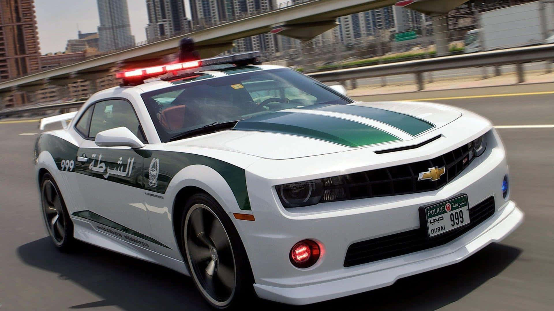Police Car 桌布 壁紙 — 一輛帶有綠色條紋的白色杜拜警車Camaro在現代城市天際線下的高速公路上疾馳。