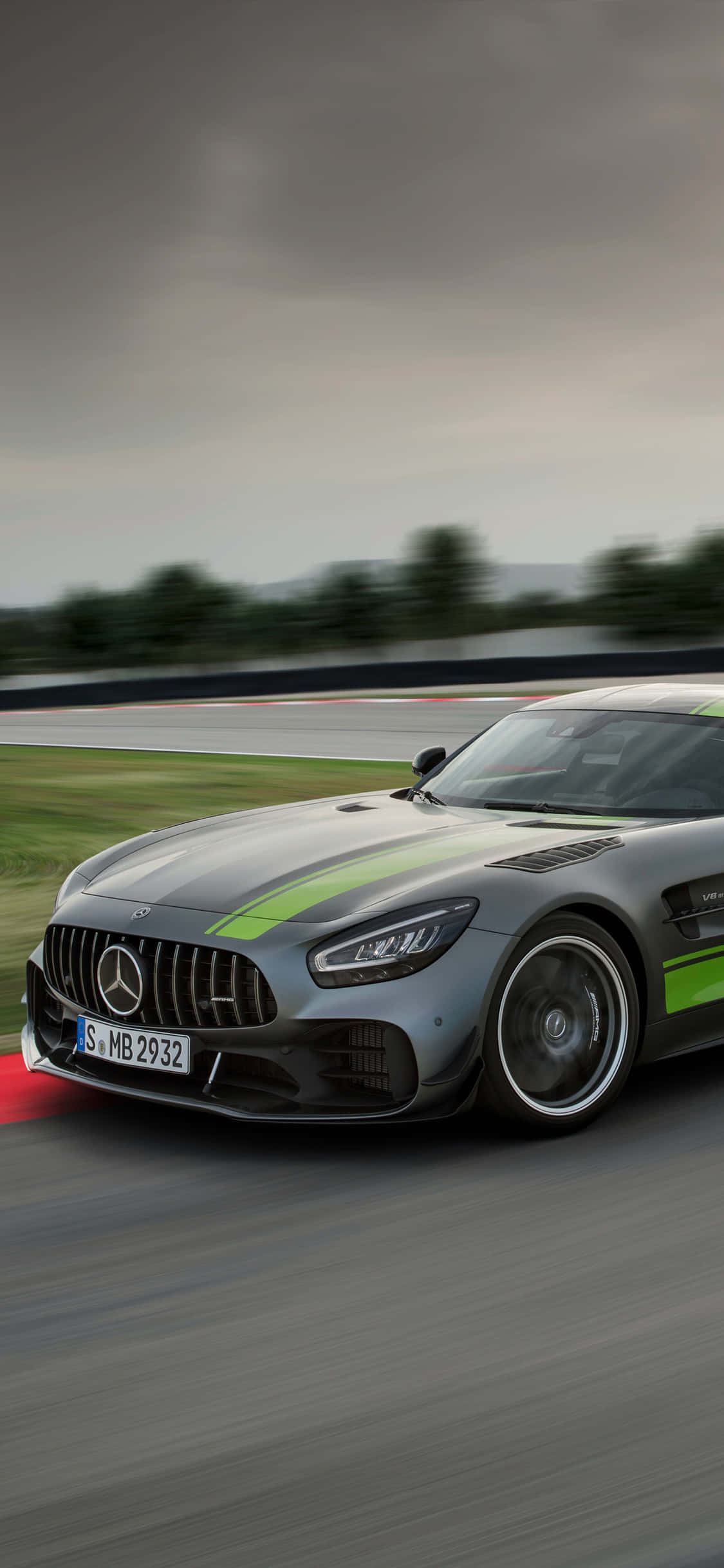 跑車 桌布 壁紙 — 一輛帶有綠色賽車條紋的時尚銀色 Mercedes-AMG GT 在多雲的天空下沿著潮濕的賽道飛馳。