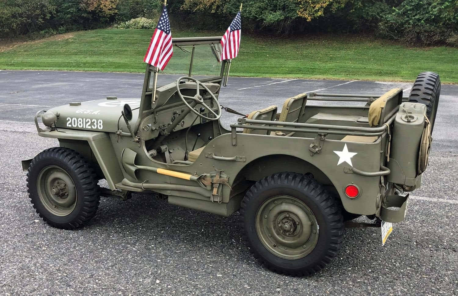Jeep Willys 桌布 壁紙 — 一輛帶有美國國旗的復古橄欖綠軍用吉普車停在碎石地上，周圍是綠草和樹木。