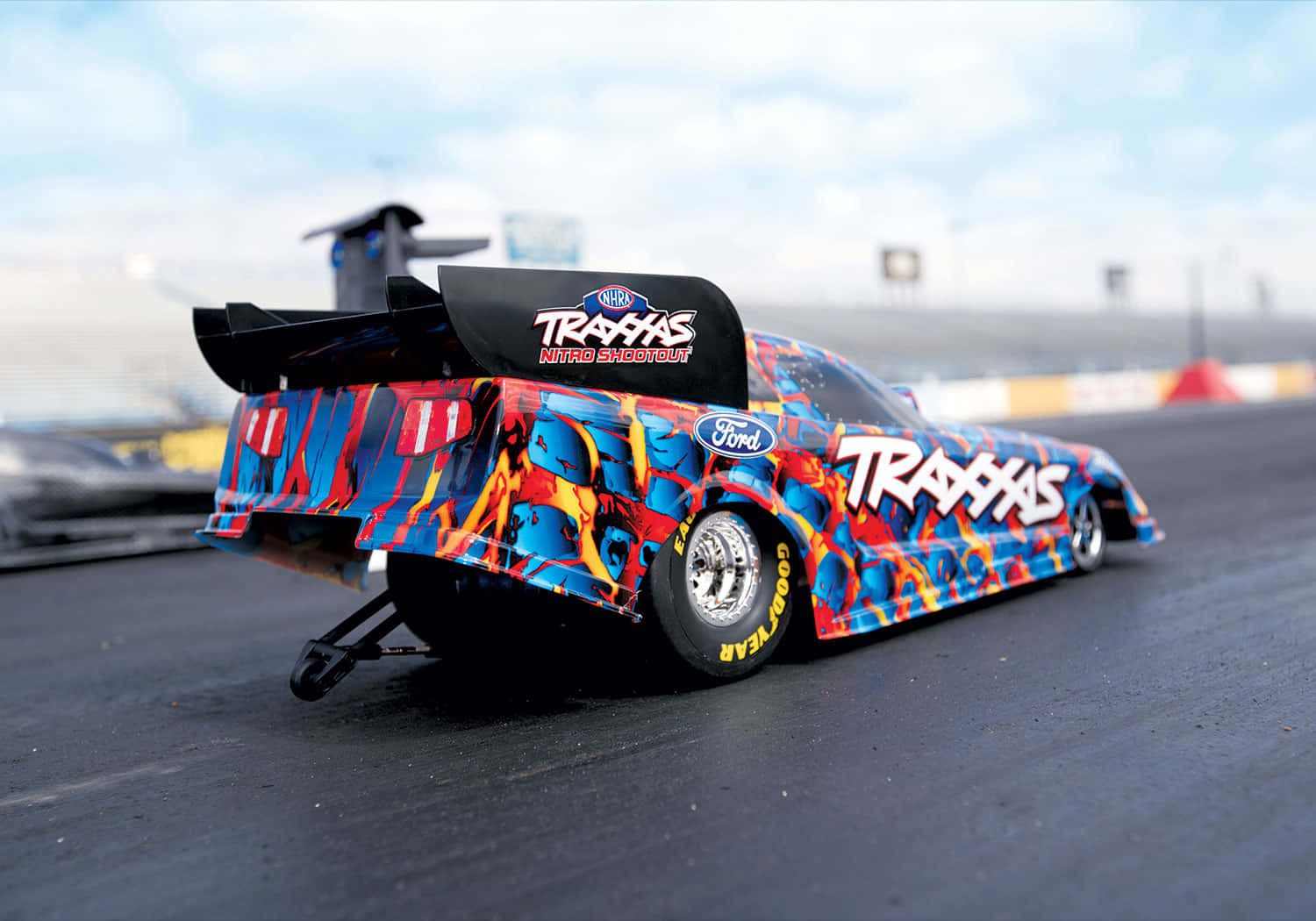 cars 桌布 壁紙 — 一輛帶有藍、紅、黃火焰塗裝、印有 'Traxxas' 品牌的鮮豔直線加速賽車，在陰天下的賽道上蓄勢待發。