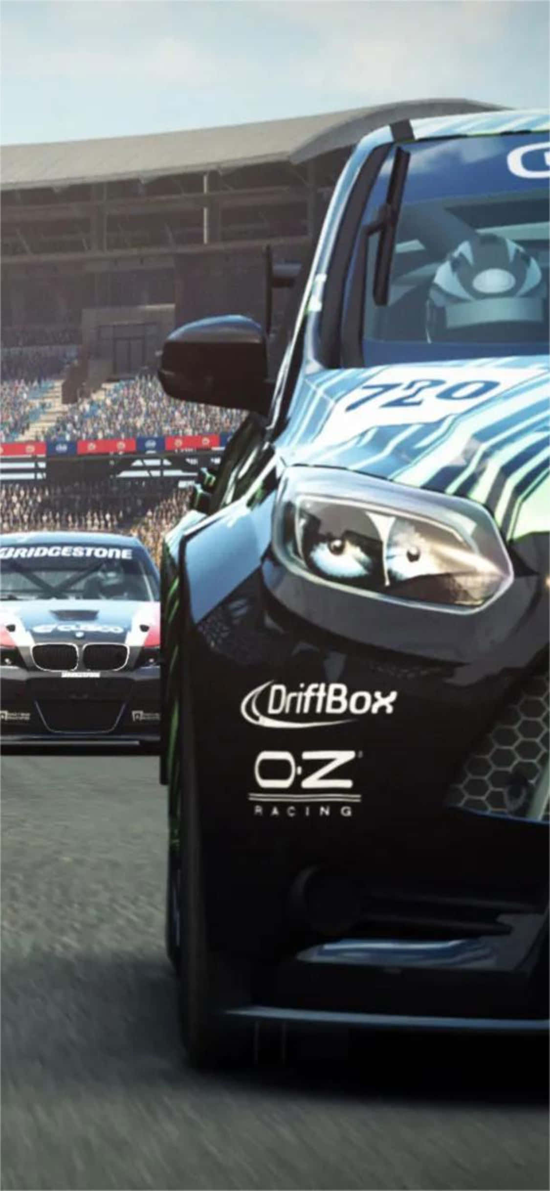 iPhone Xs Grid Autosport 桌布 壁紙 — 一輛帶有藍白圖案的黑色賽車在賽道上飄移，背景有觀眾。