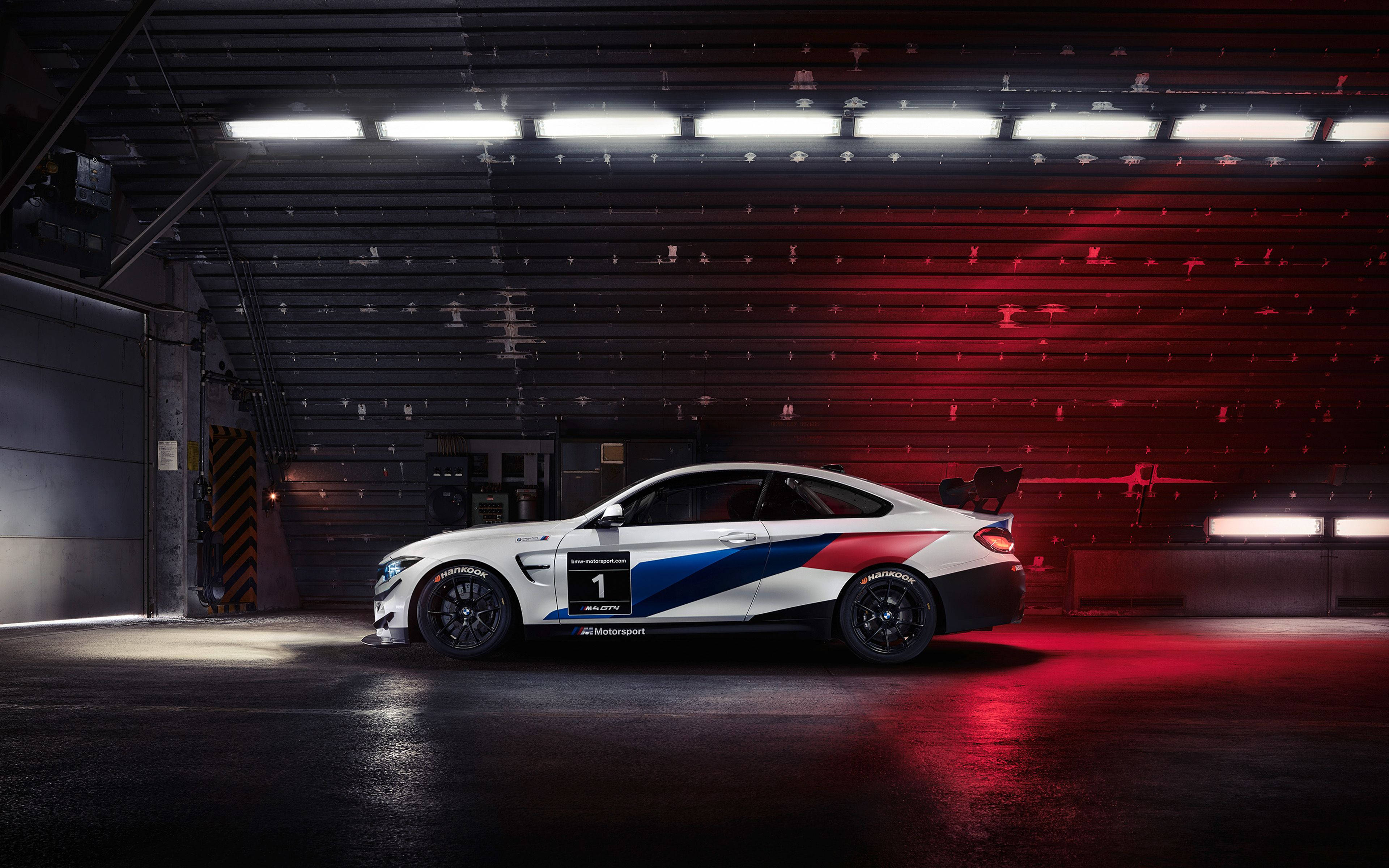 BMW 動圖 桌布 壁紙 — 一輛帶有藍紅塗裝的白色BMW M2賽車停在昏暗的車庫中，沐浴在紅光下。