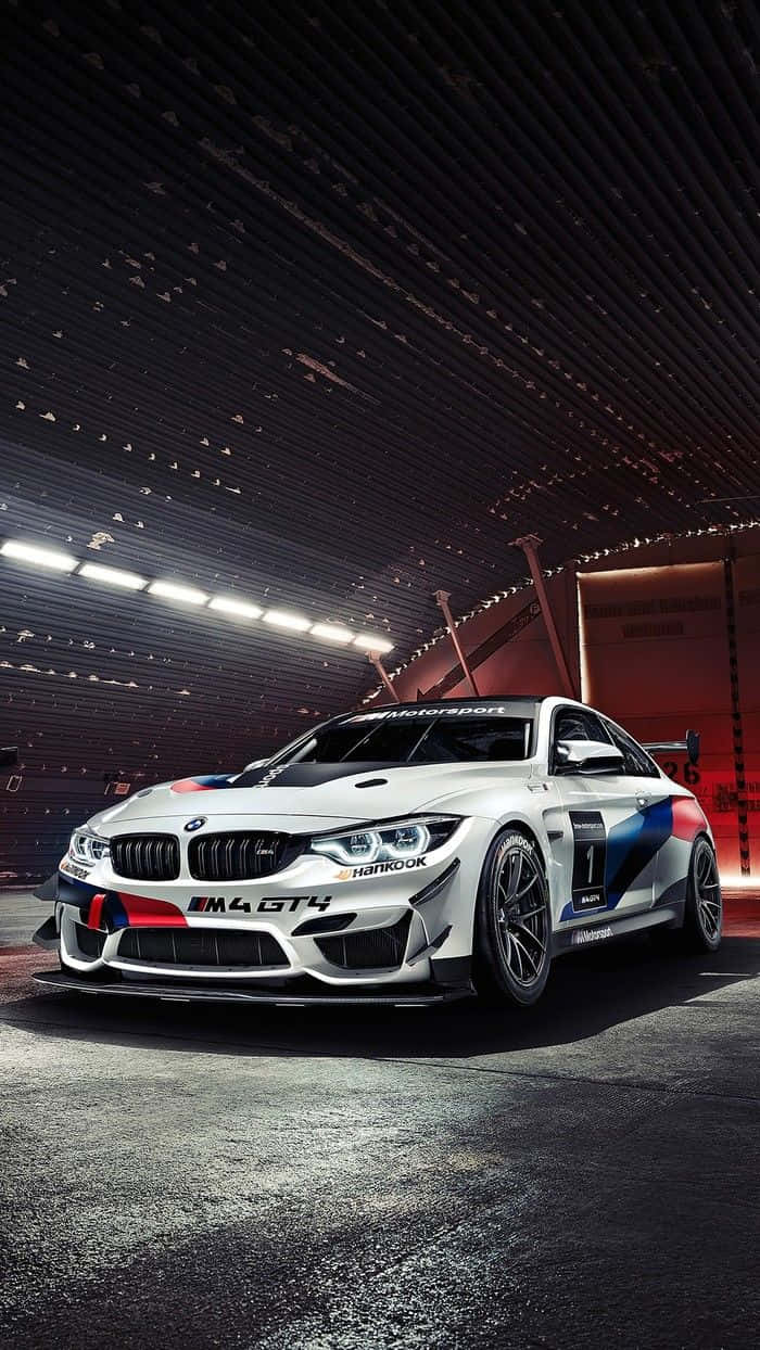 Bmw M8 4K 桌布 壁紙 — 一輛帶有藍紅飾邊的白色BMW M4 GT4賽車，在明亮的燈光下，停放在時尚的暗色車庫中。