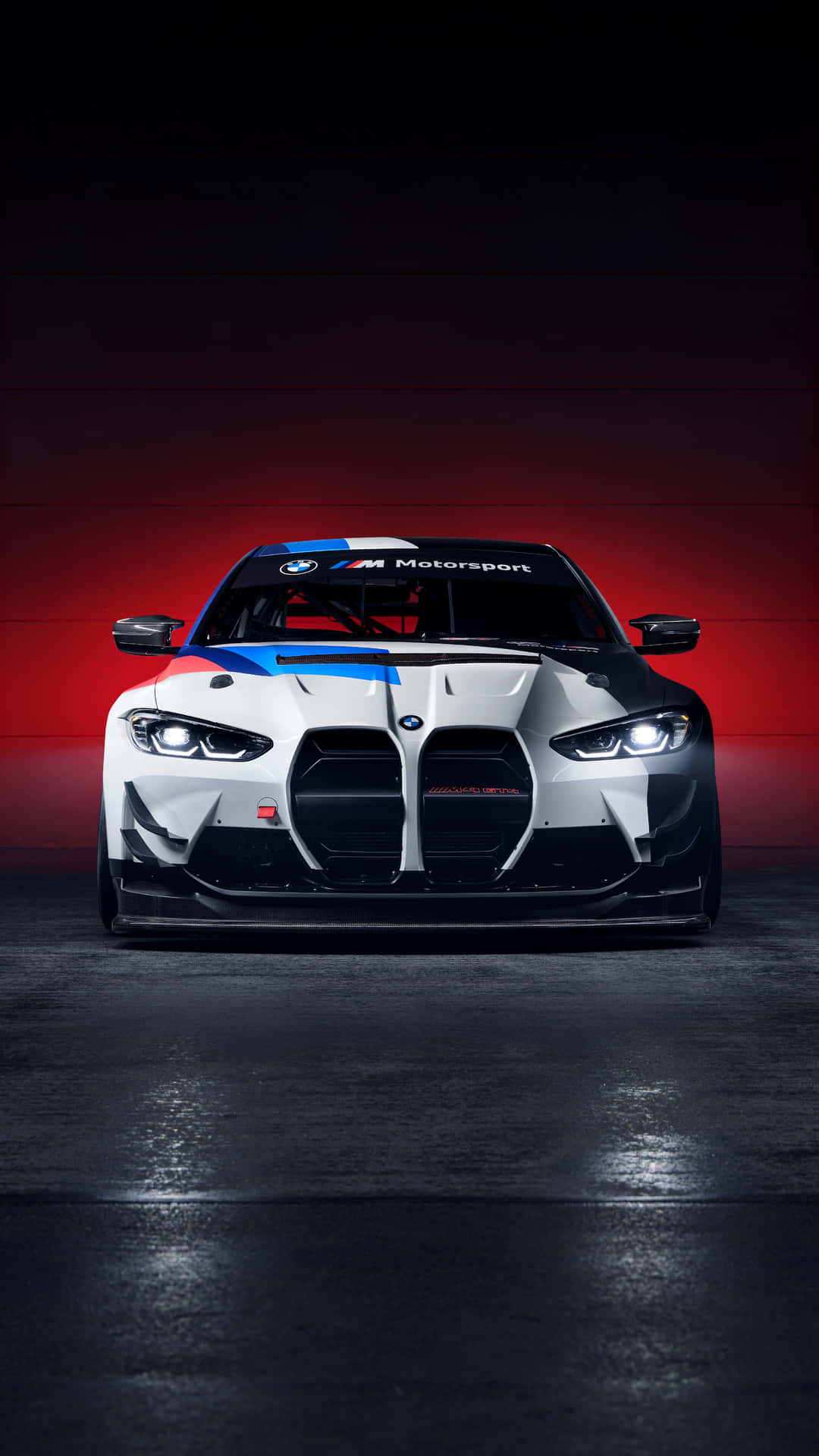 Bmw M8 4K 桌布 壁紙 — 一輛帶有藍色和紅色點綴的白色BMW M Motorsport賽車，在黑暗車庫中戲劇性的紅色燈光下直視前方。