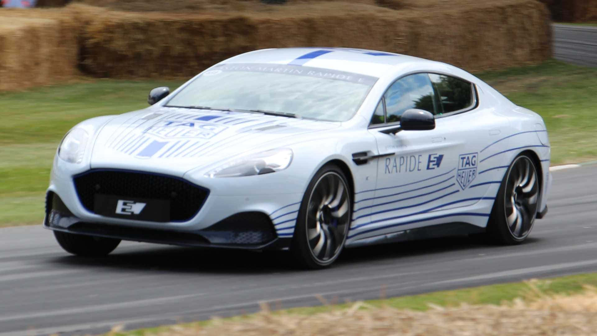 Aston Martin Rapide S 桌布 壁紙 — 一輛帶有藍色賽車條紋的白色Aston Martin Rapide E在由乾草捆和綠草環繞的賽道上飛馳。