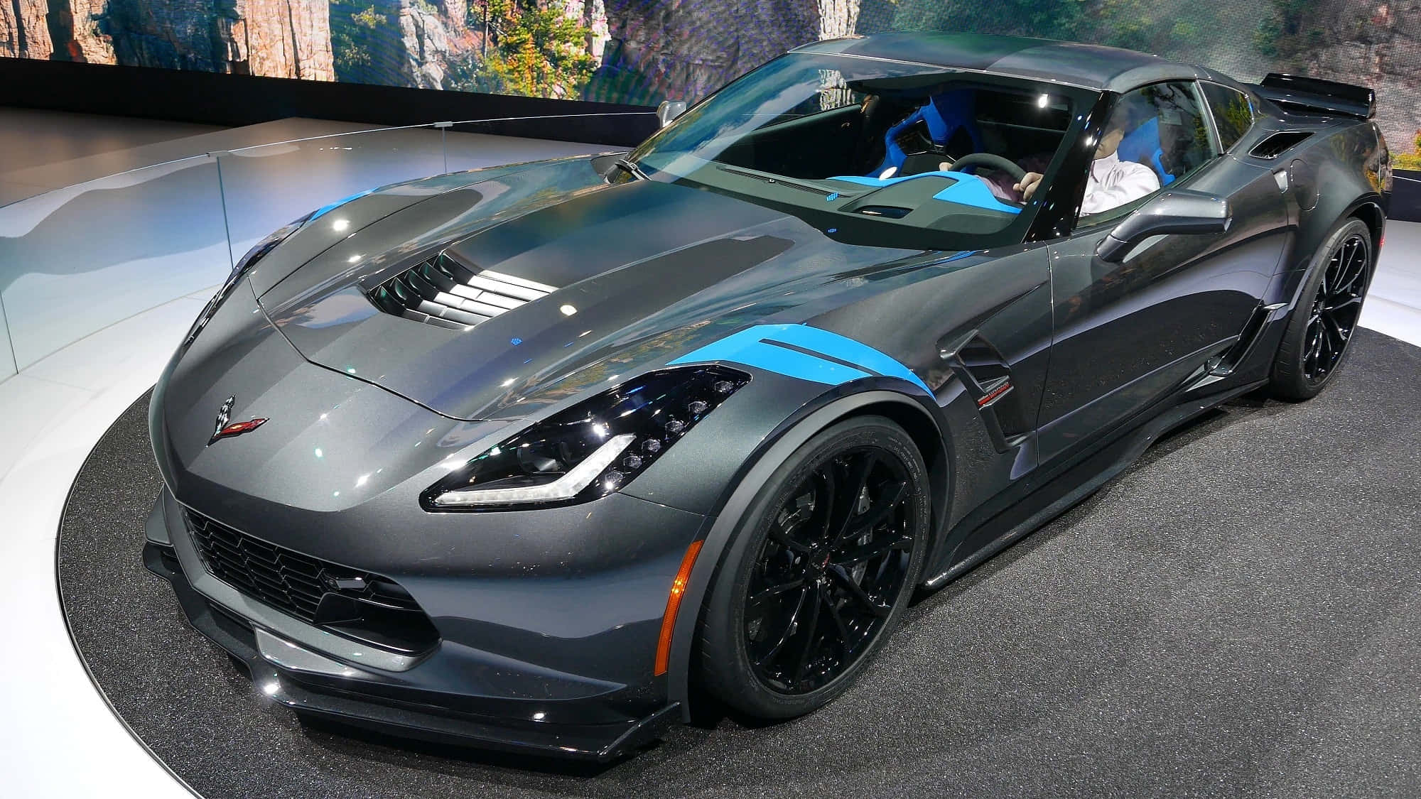 Chevrolet 桌布 壁紙 — 一輛帶有藍色點綴的時尚灰色Corvette跑車在車展的旋轉平台上展示。