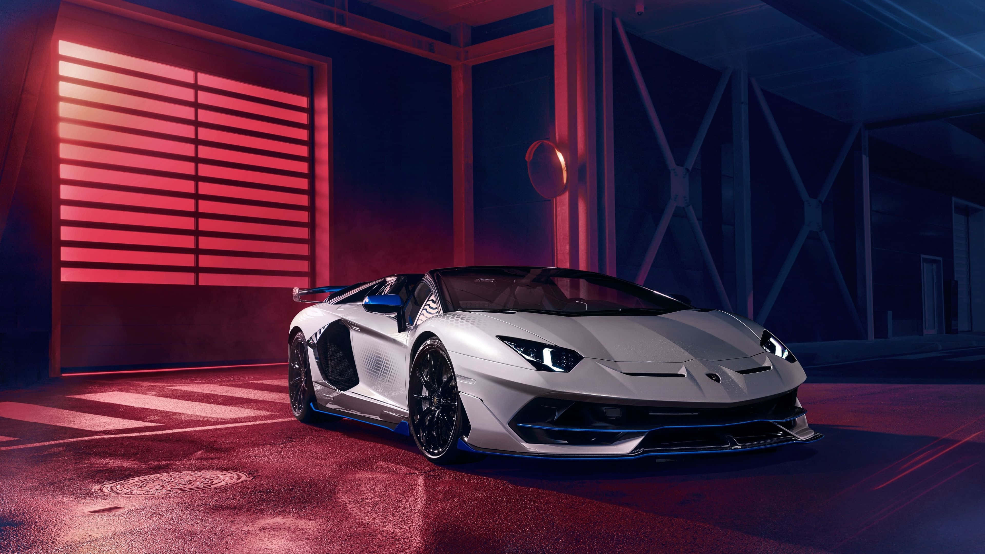 4K 藍寶堅尼 桌布 壁紙 — 一輛帶有藍色點綴的時尚銀色藍寶堅尼 Aventador SVJ 在現代車庫中，於戲劇性的紅色和藍色燈光下閃耀。