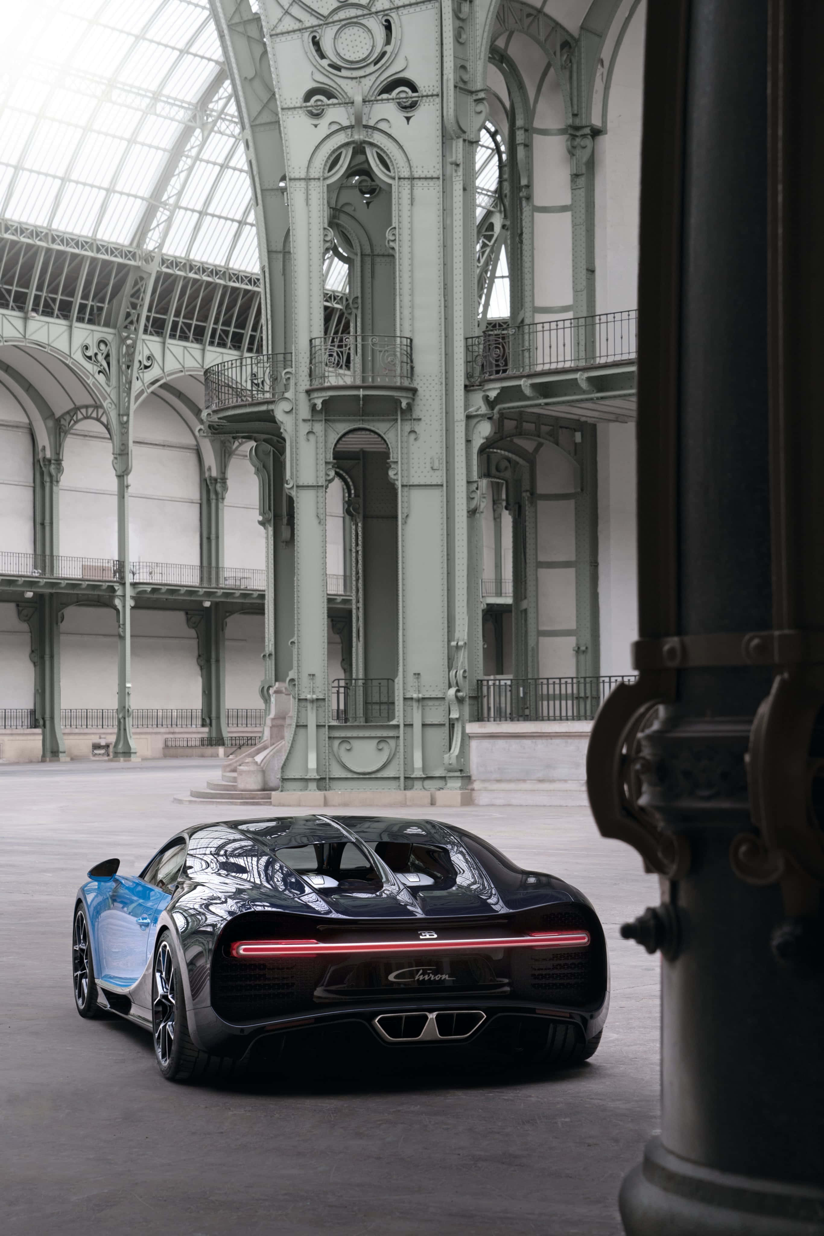 Bugatti Phone 桌布 壁紙 — 一輛帶有藍色點綴的時尚黑色Bugatti Chiron停放在一座裝飾華麗的玻璃和鐵製大廳內。