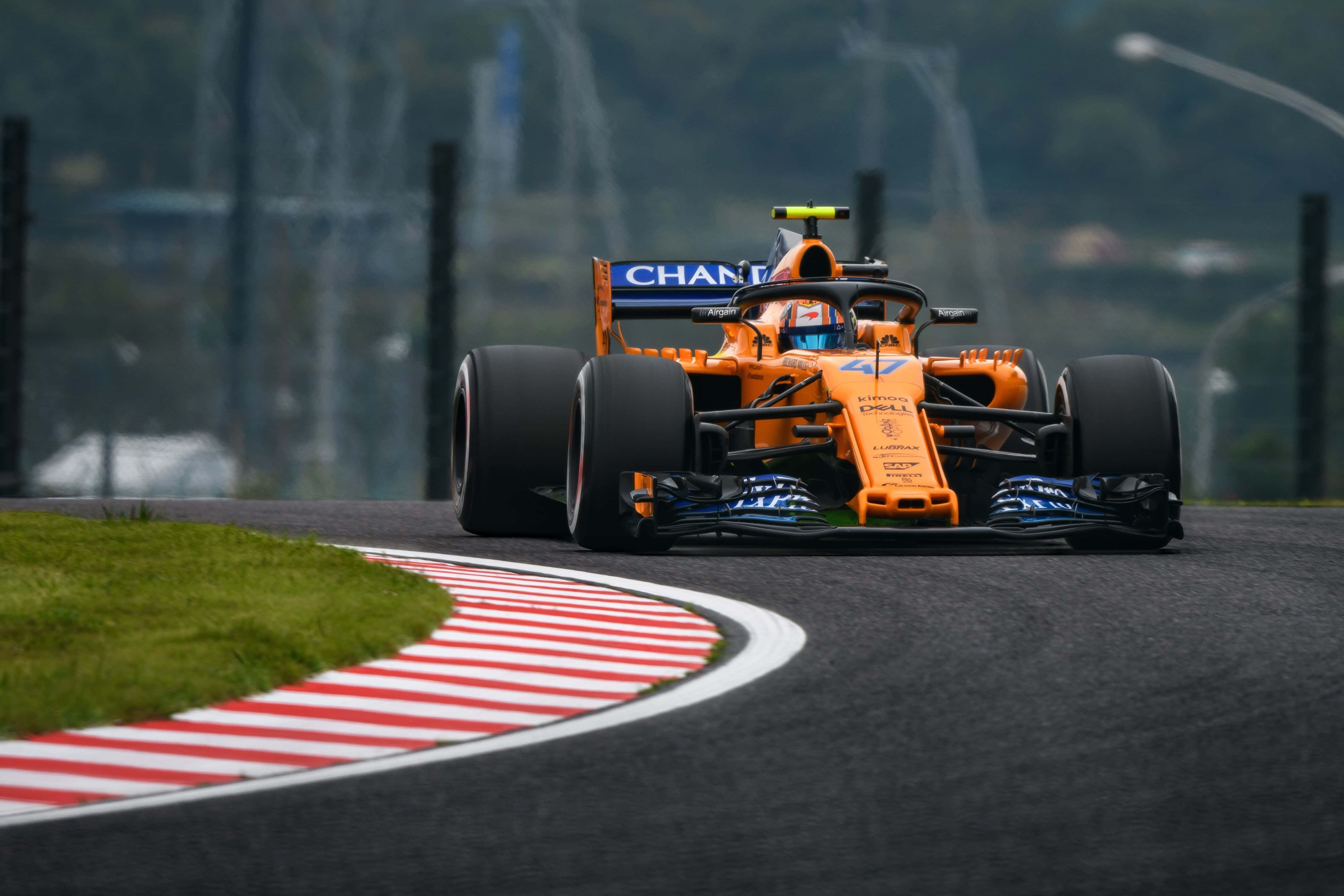 lando norris 桌布 壁紙 — 一輛帶有藍色點綴的橙色一級方程式賽車在紅白路肩環繞的濕滑賽道彎道上疾馳。
