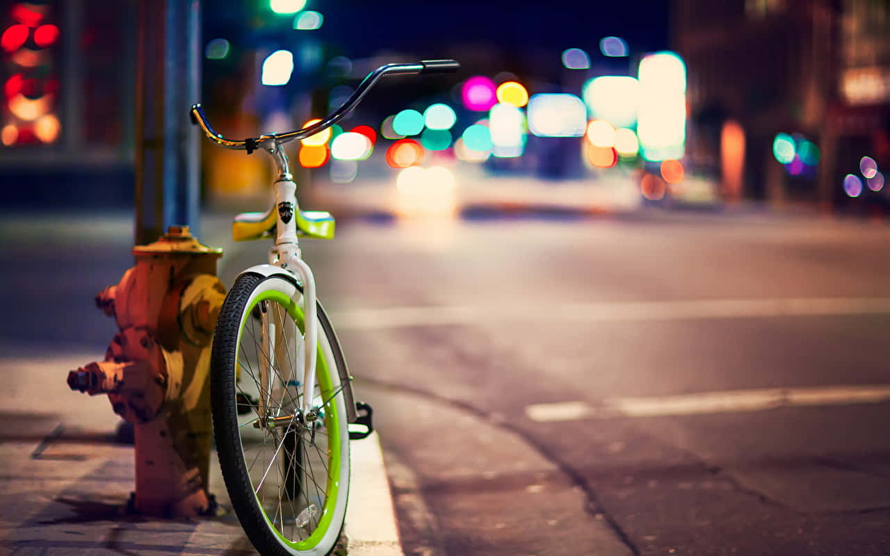 Bicycle 桌布 壁紙 — 一輛帶有螢光綠色點綴的白色自行車靠在城市人行道上的消防栓旁，在充滿活力的夜間散景燈光下。