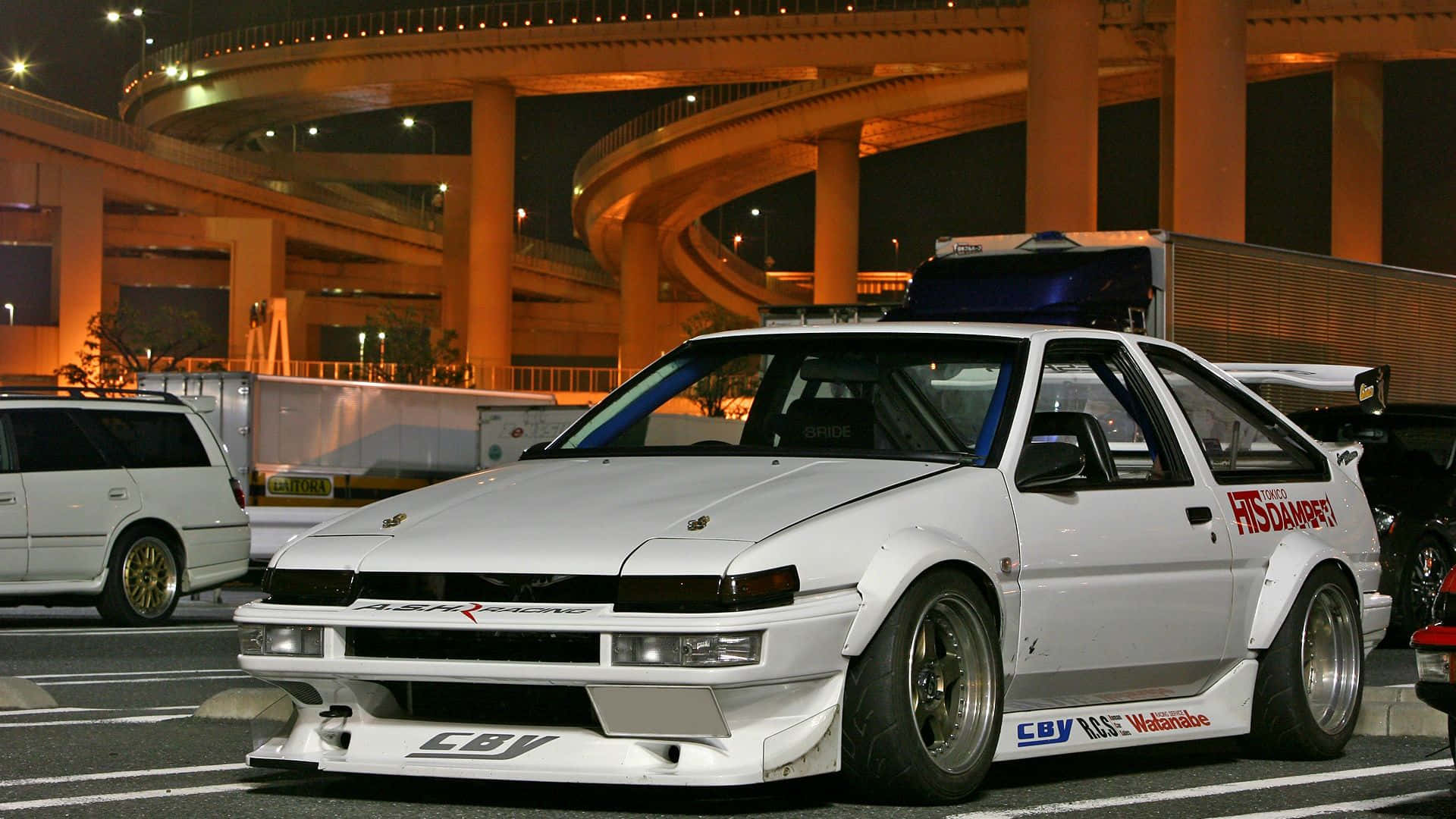 桌布 壁紙 — 一輛帶有賽車貼紙的白色改裝AE86跑車，夜間停放在發光的橙色高速公路高架橋下。