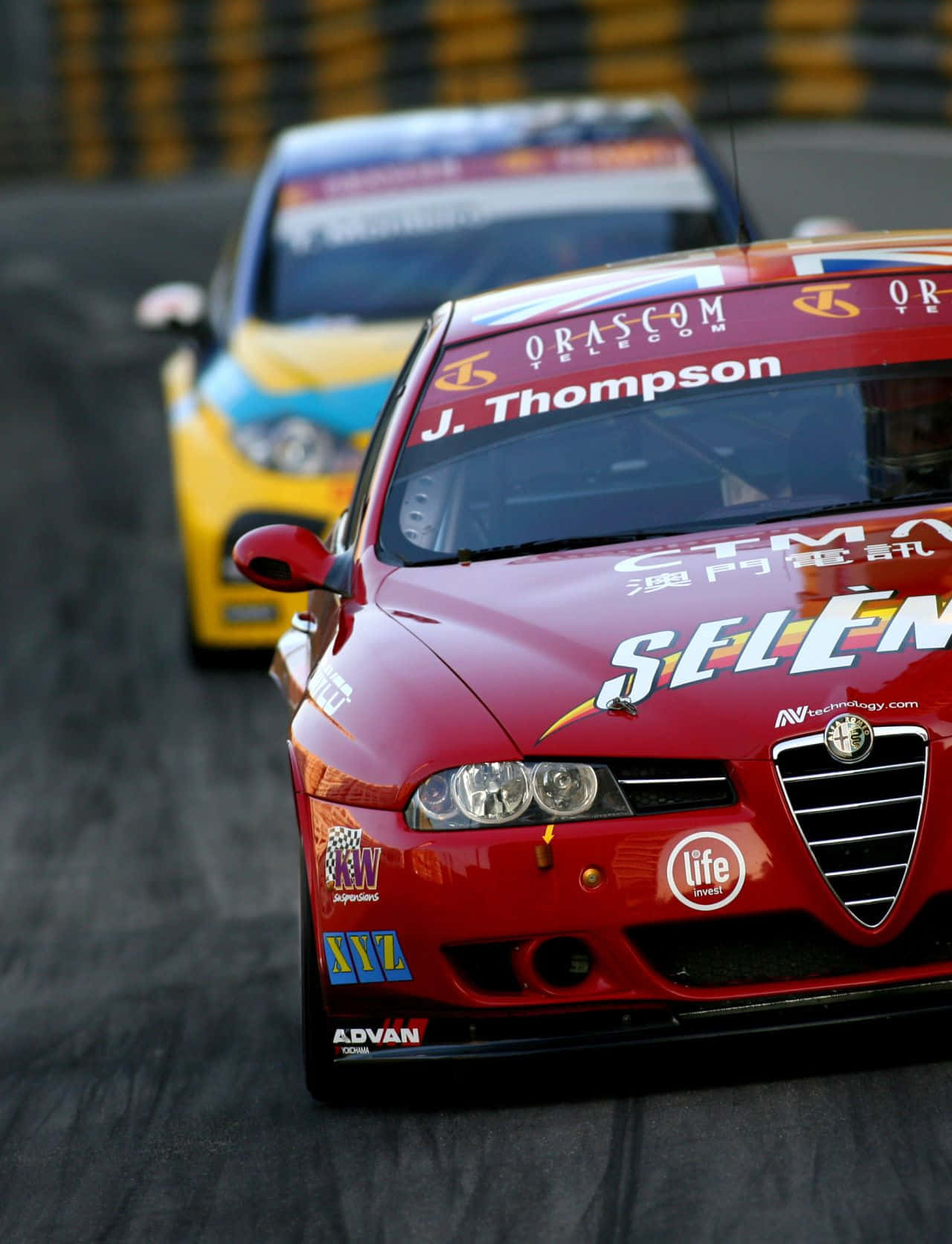 Alfa Romeo 156 桌布 壁紙 — 一輛帶有贊助商貼紙的紅色愛快羅密歐賽車在賽道上奔馳，背景中有一輛黃色汽車模糊不清。