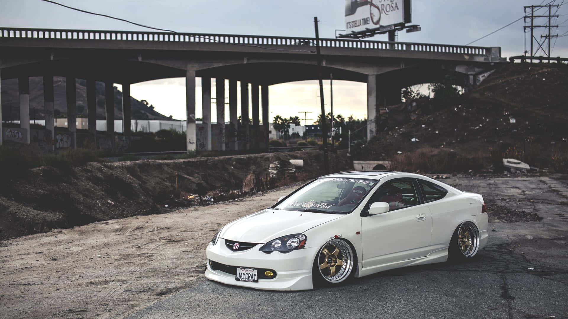 Acura Integra 桌布 壁紙 — 一輛帶有金色輪圈的純白色改裝跑車停在城市路邊的混凝土天橋下。
