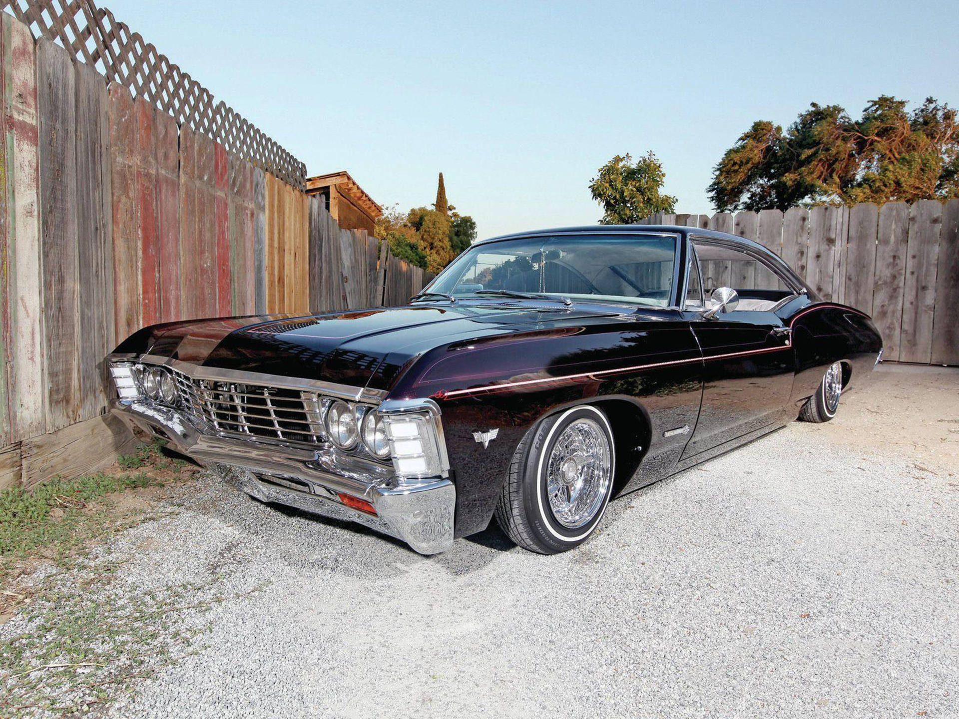 chevrolet impala 1967 桌布 壁紙 — 一輛帶有鍍鉻細節的亮黑色經典美國肌肉車停在碎石上，旁邊是風化的木柵欄，背景是清澈的藍天。
