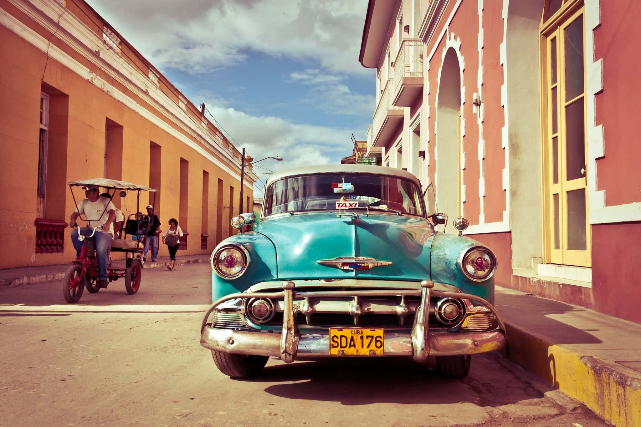Cuba 桌布 壁紙 — 一輛帶有鍍鉻細節的復古青綠色計程車停在古巴陽光明媚的街道上，兩旁是色彩繽紛的殖民時期建築。