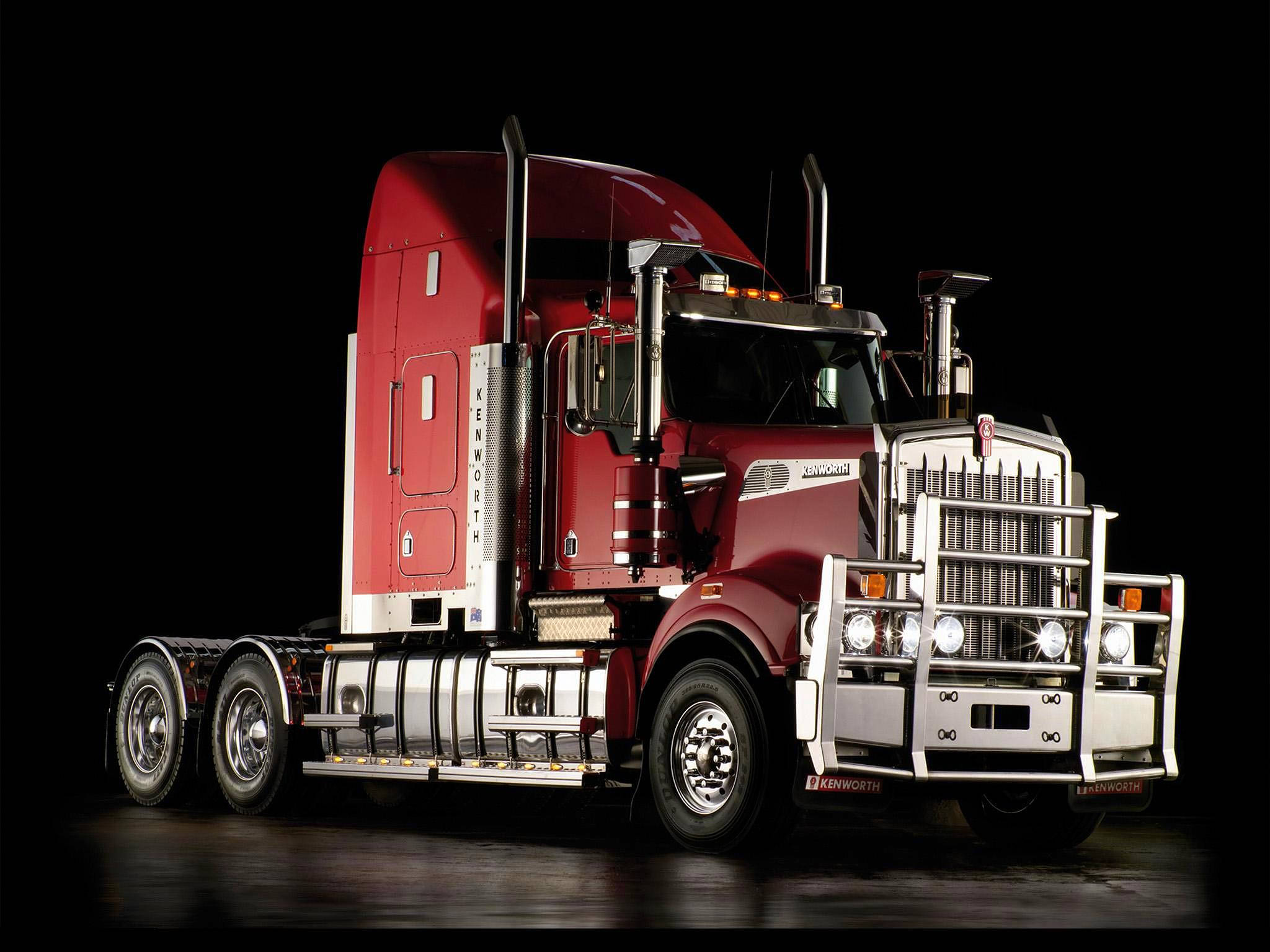 Kenworth 桌布 壁紙 — 一輛帶有鍍鉻裝飾的亮紅色Kenworth半掛卡車在黑色工作室背景下大膽矗立，車頭燈閃爍。