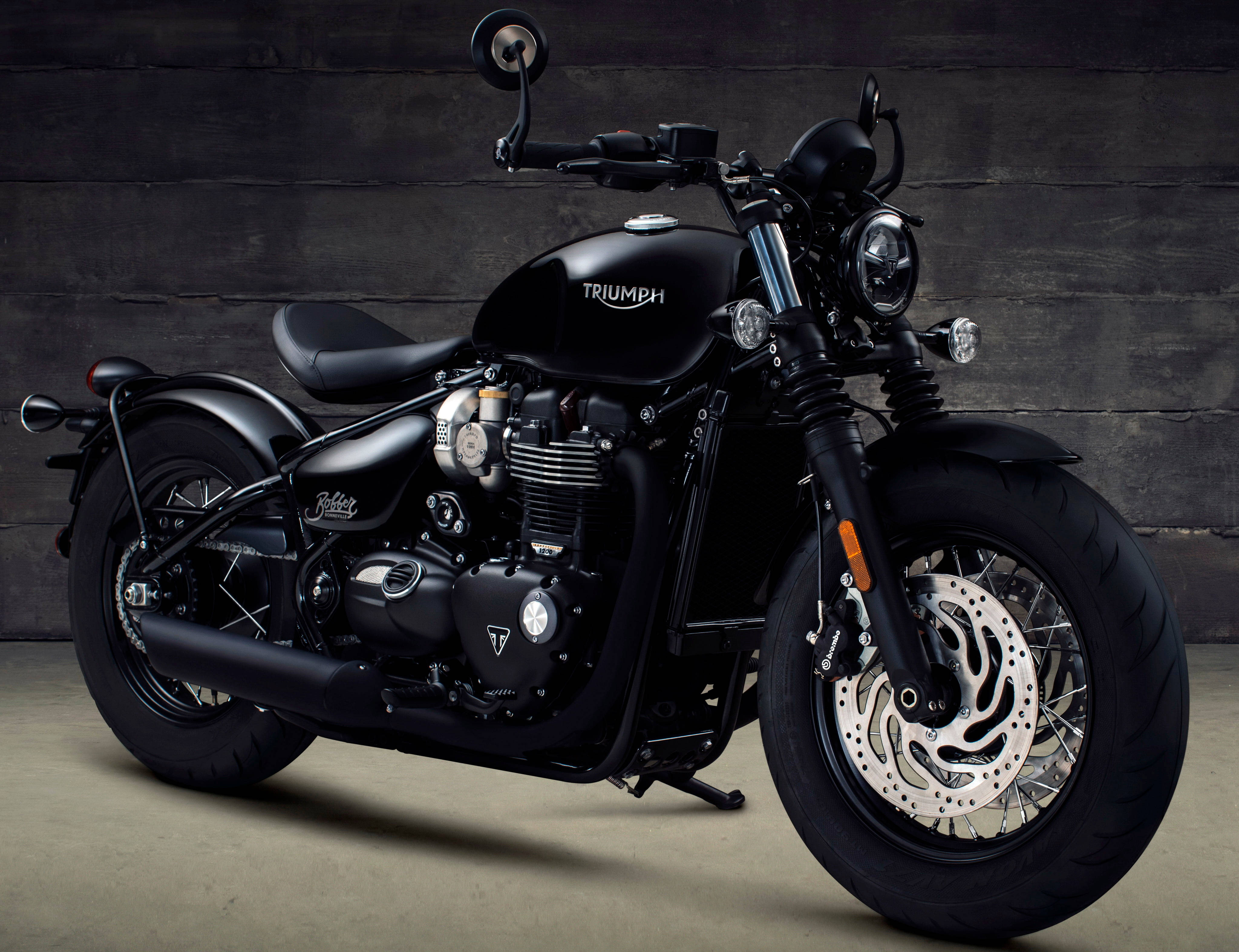 Bobber 桌布 壁紙 — 一輛帶有鍍鉻裝飾的時尚黑色Triumph機車，在攝影棚環境中靠著深色木牆停放。