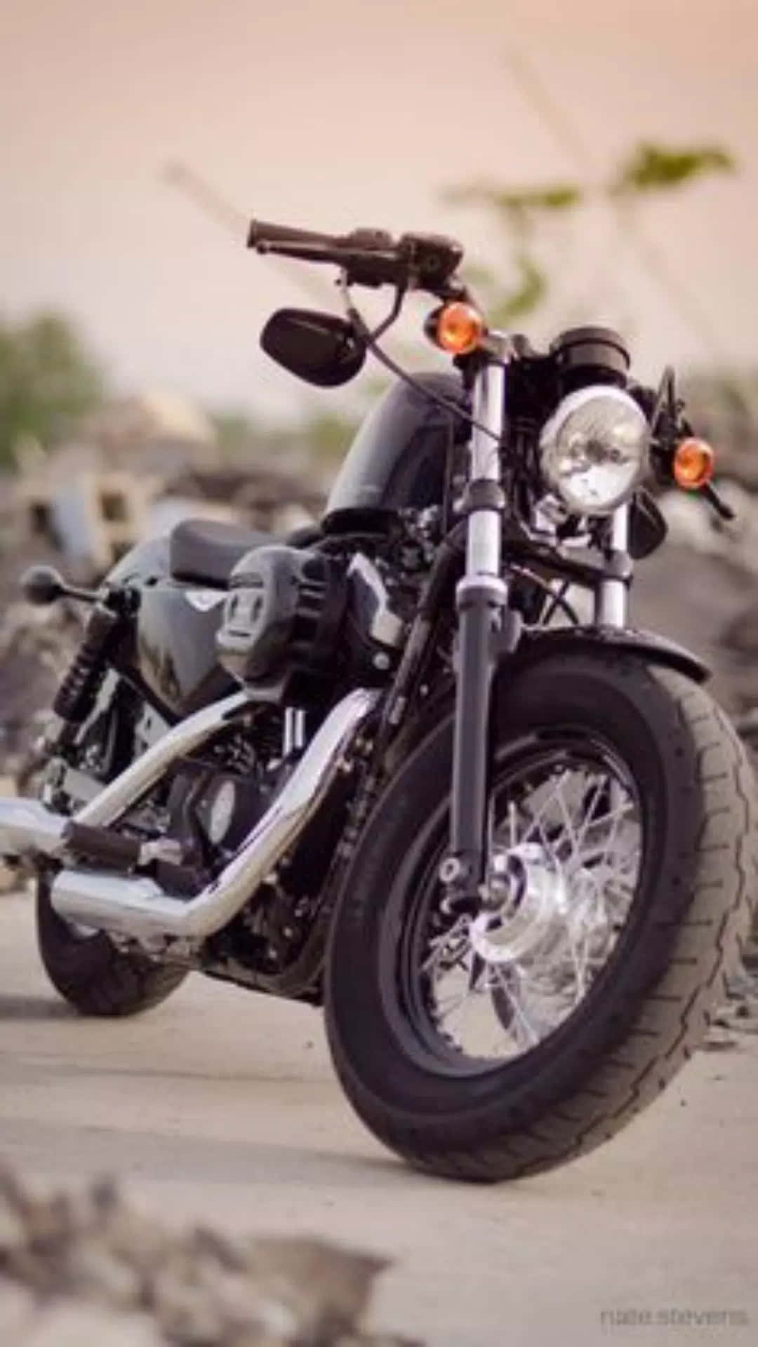 Harley Davidson HD 桌布 壁紙 — 一輛帶有鍍鉻裝飾的時尚黑色摩托車，在溫暖的金色天空下停泊在碎石路上。