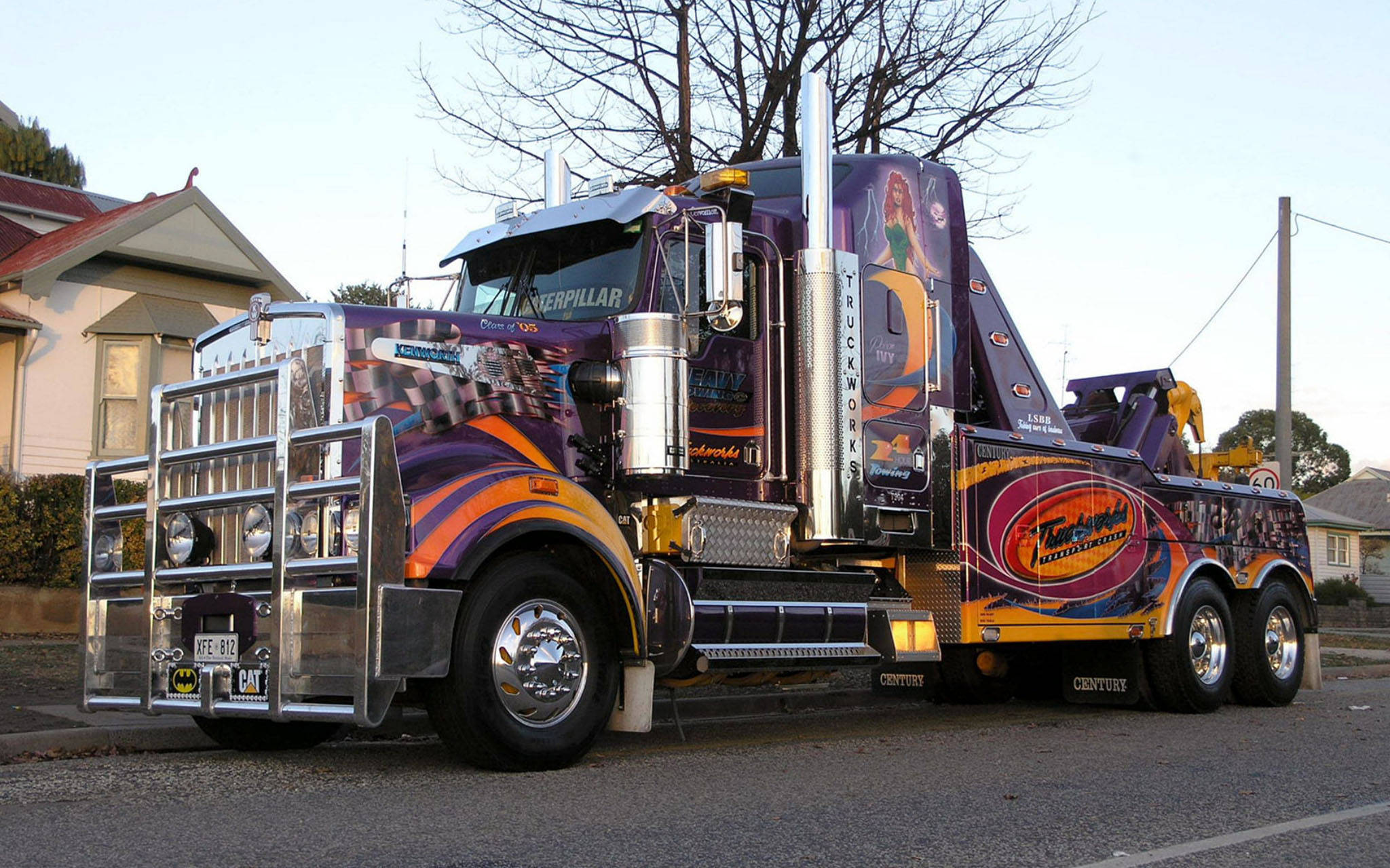 Kenworth W900 桌布 壁紙 — 一輛帶有鍍鉻裝飾的鮮豔紫色和橙色定制拖車，在黎明時分停放在住宅街道上。