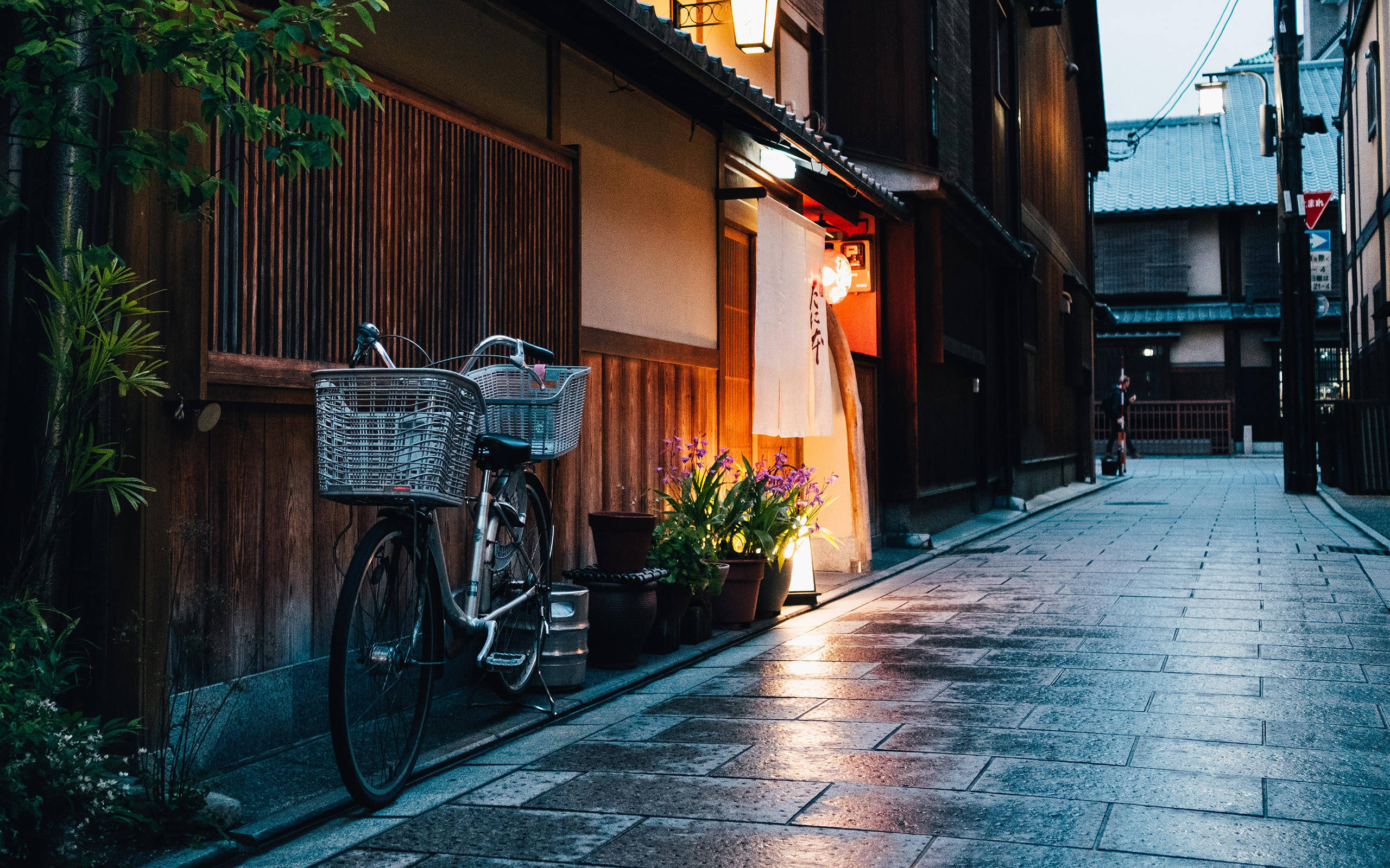 Bicycle 桌布 壁紙 — 一輛帶有鐵絲籃的復古自行車靠在木建築上，位於一條寧靜的日本小巷中，黃昏時分被溫暖的燈籠照亮。