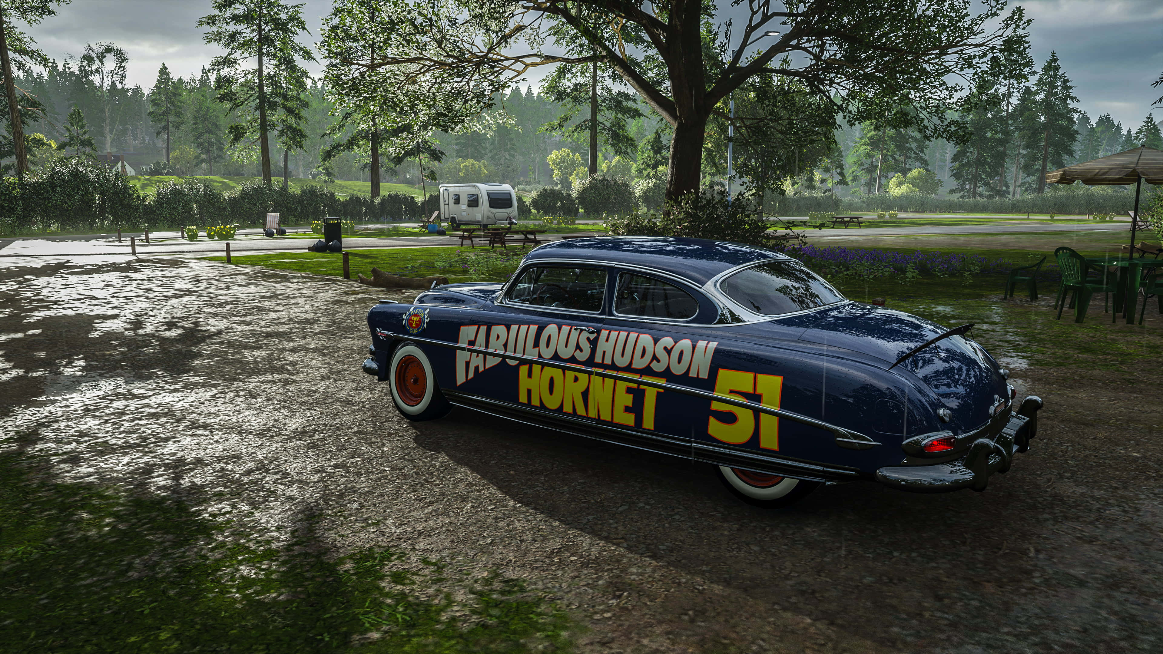 Forza Horizon 桌布 壁紙 — 一輛帶有黃色字樣的復古藍色Fabulous Hudson Hornet賽車停放在潮濕的碎石地上，天空多雲。