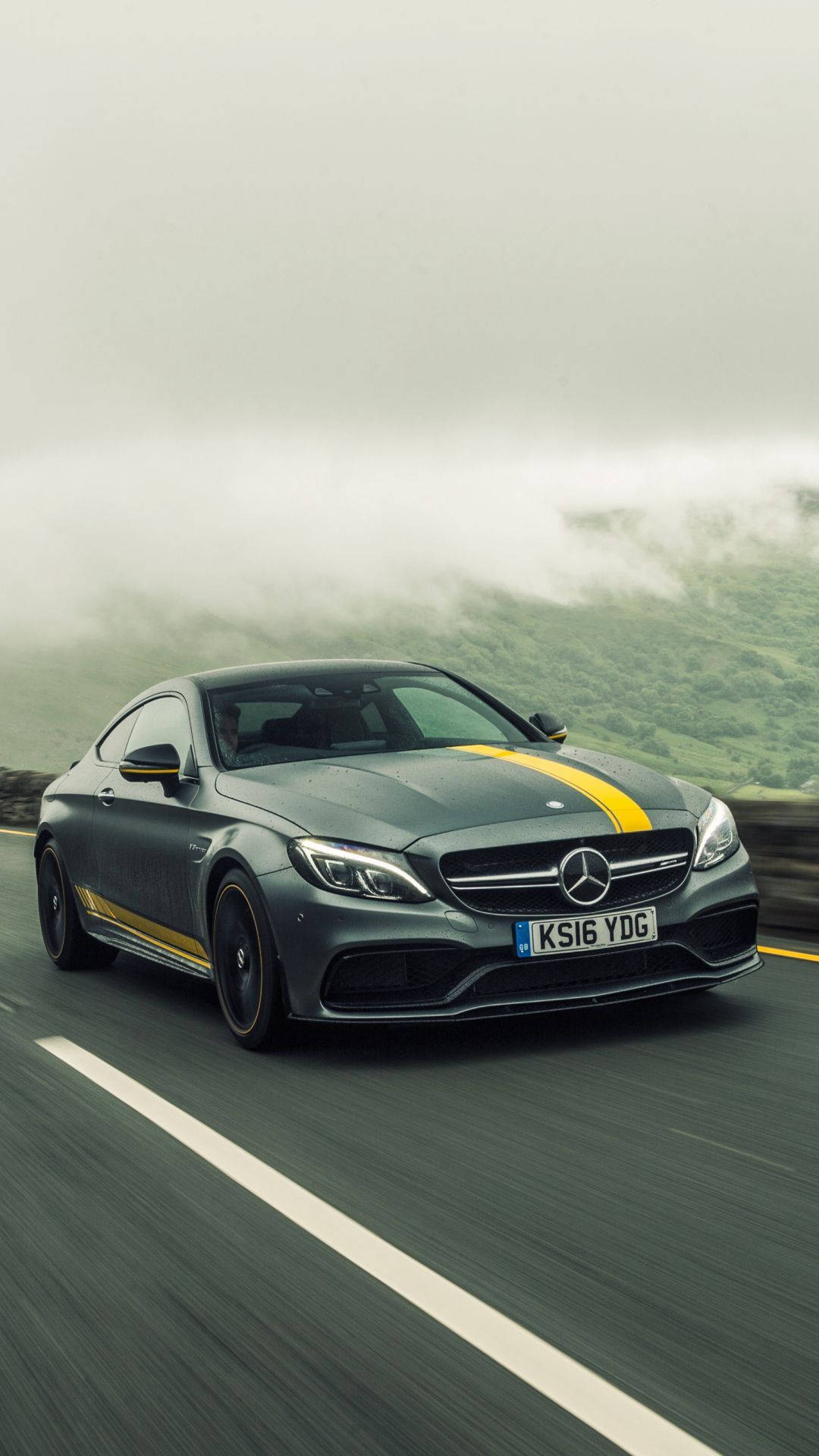 AMG iPhone 桌布 壁紙 — 一輛帶有黃色條紋的時尚灰色 Mercedes-AMG C63 S 雙門跑車在霧氣瀰漫的山路上疾馳。