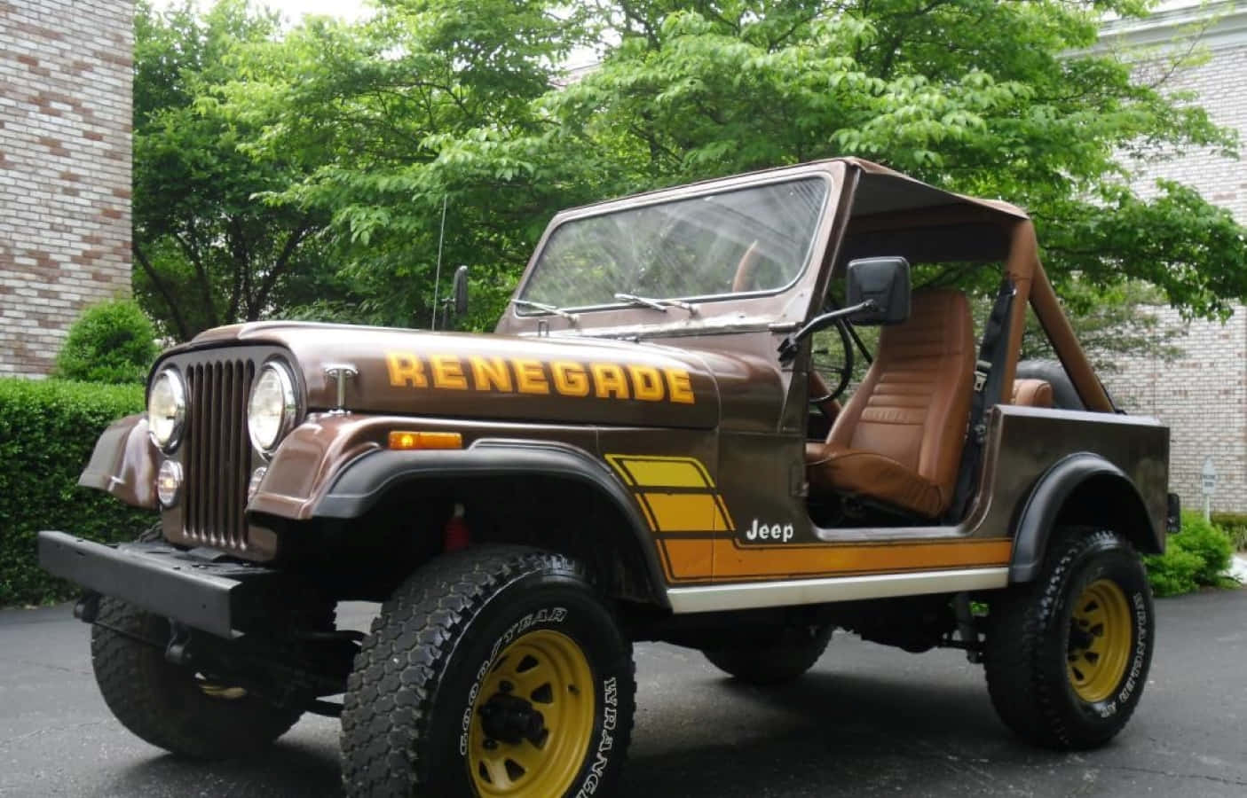 Jeep Cj 桌布 壁紙 — 一輛帶有黃色點綴和米色內裝的棕色Jeep Renegade停在柏油路上，周圍環繞著綠樹和磚造建築。