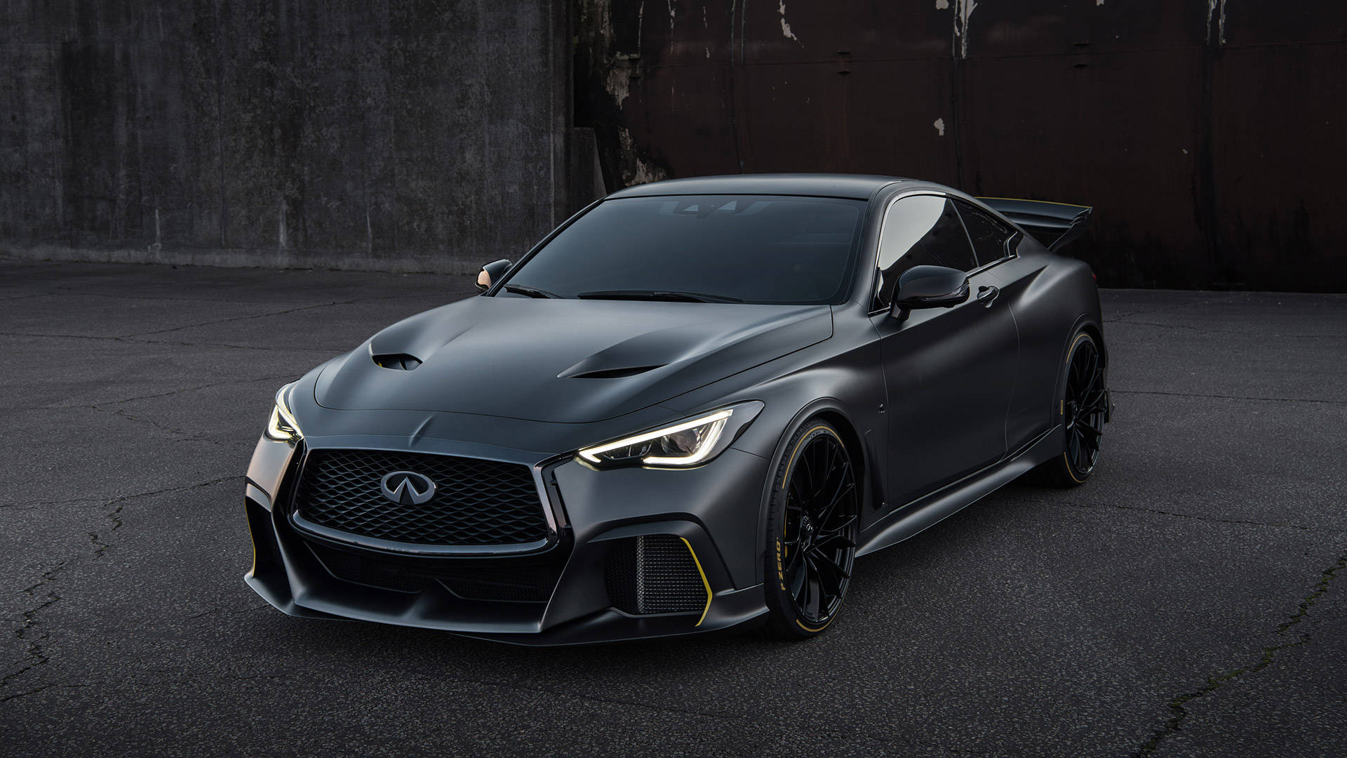 Infiniti 桌布 壁紙 — 一輛帶有黃色點綴的消光黑色 Infiniti 跑車，停在裂開的柏油路面上，背景是風化的混凝土牆。