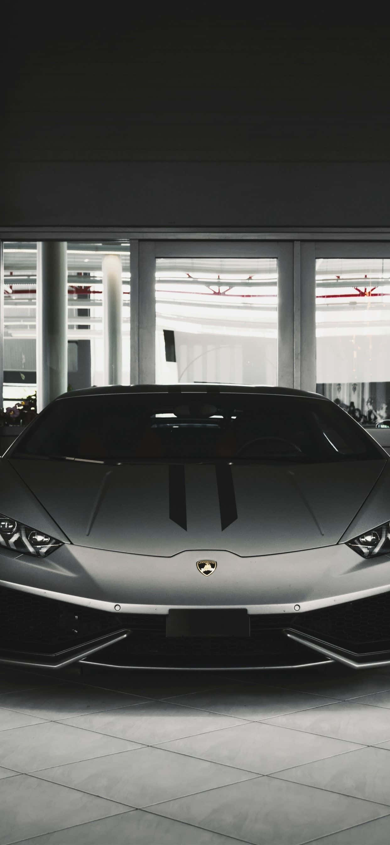 跑車 桌布 壁紙 — 一輛帶有黑色條紋的時尚銀色藍寶堅尼跑車，在現代簡約的展示間中展示，地板鋪有瓷磚，並設有大窗戶。