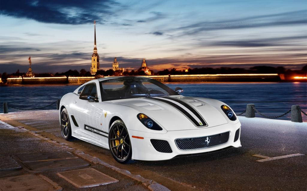 white ferrari 桌布 壁紙 — 一輛帶有黑色條紋的白色法拉利跑車停在海濱碼頭上，夕陽西下，歷史悠久的尖塔在背景中閃耀。