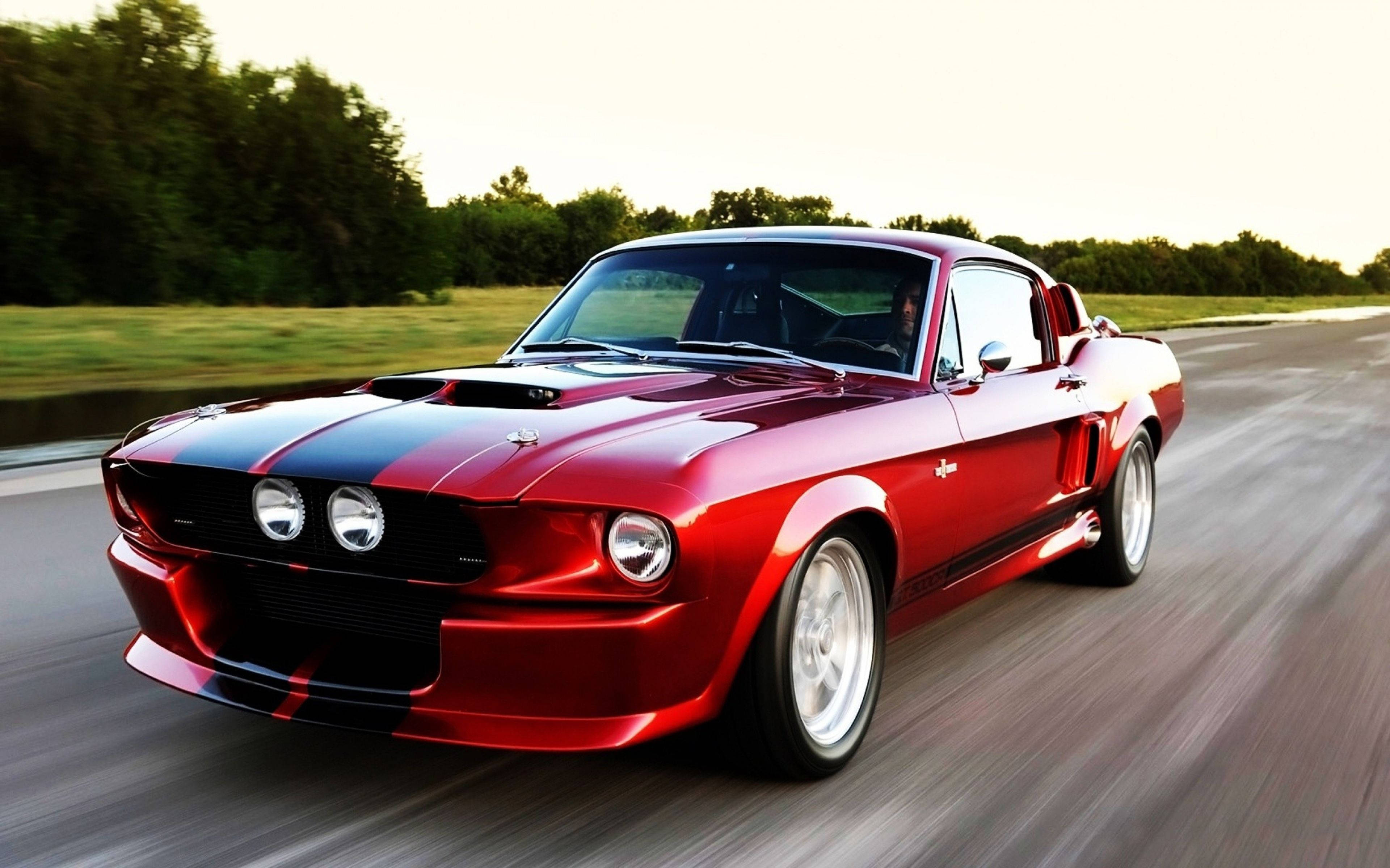 mustang HD 桌布 壁紙 — 一輛帶有黑色條紋的鮮紅色經典肌肉車在日落時分的鄉村道路上飛馳。