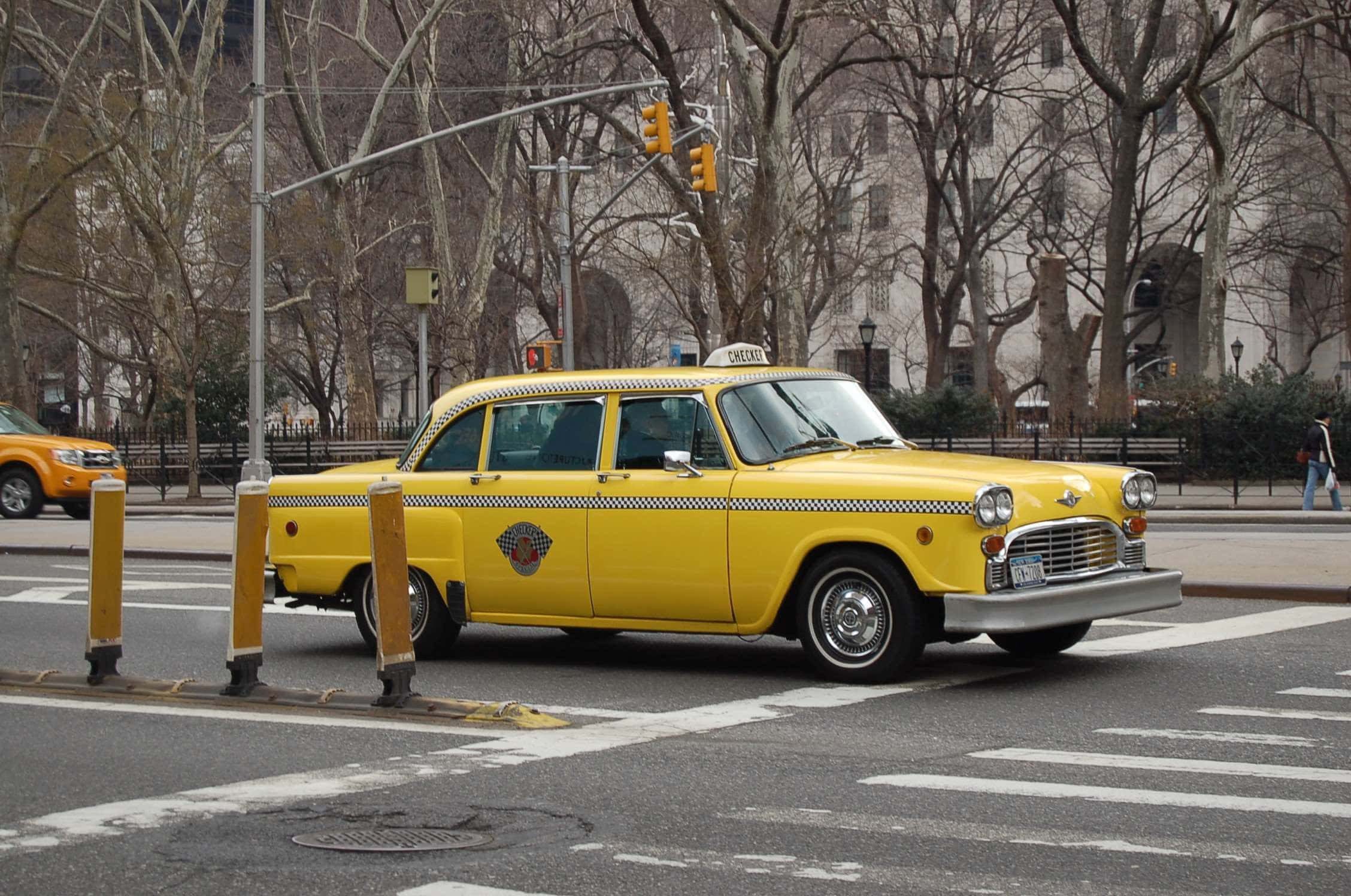 Yellow Cab 桌布 壁紙 — 一輛帶有黑色棋盤格條紋的復古黃色計程車在佈滿光禿樹木的城市交叉口等待。