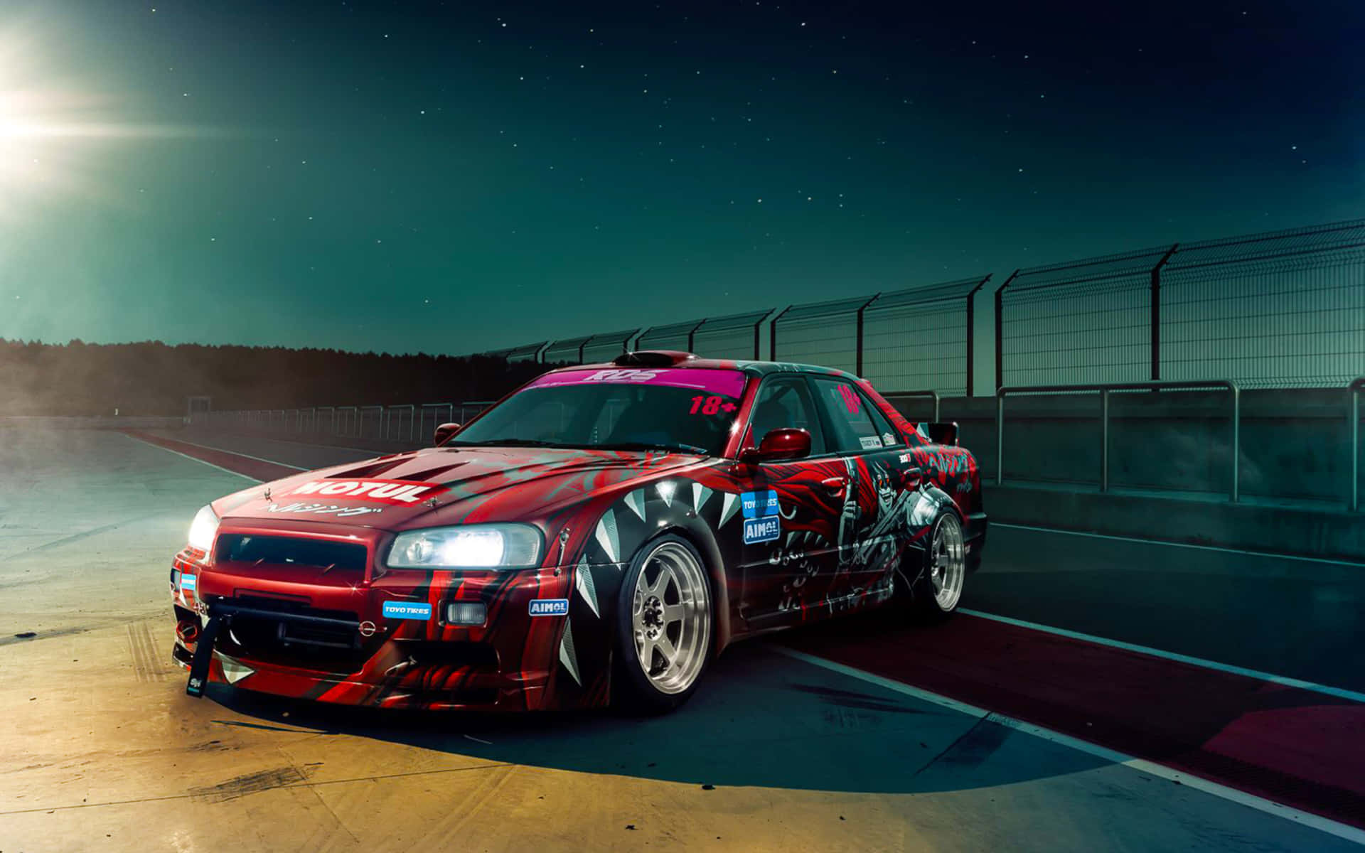 R33 GT-R 桌布 壁紙 — 一輛帶有黑色火焰貼紙的紅色甩尾車在星空下夜間賽道上奔馳，車頭燈閃閃發光。